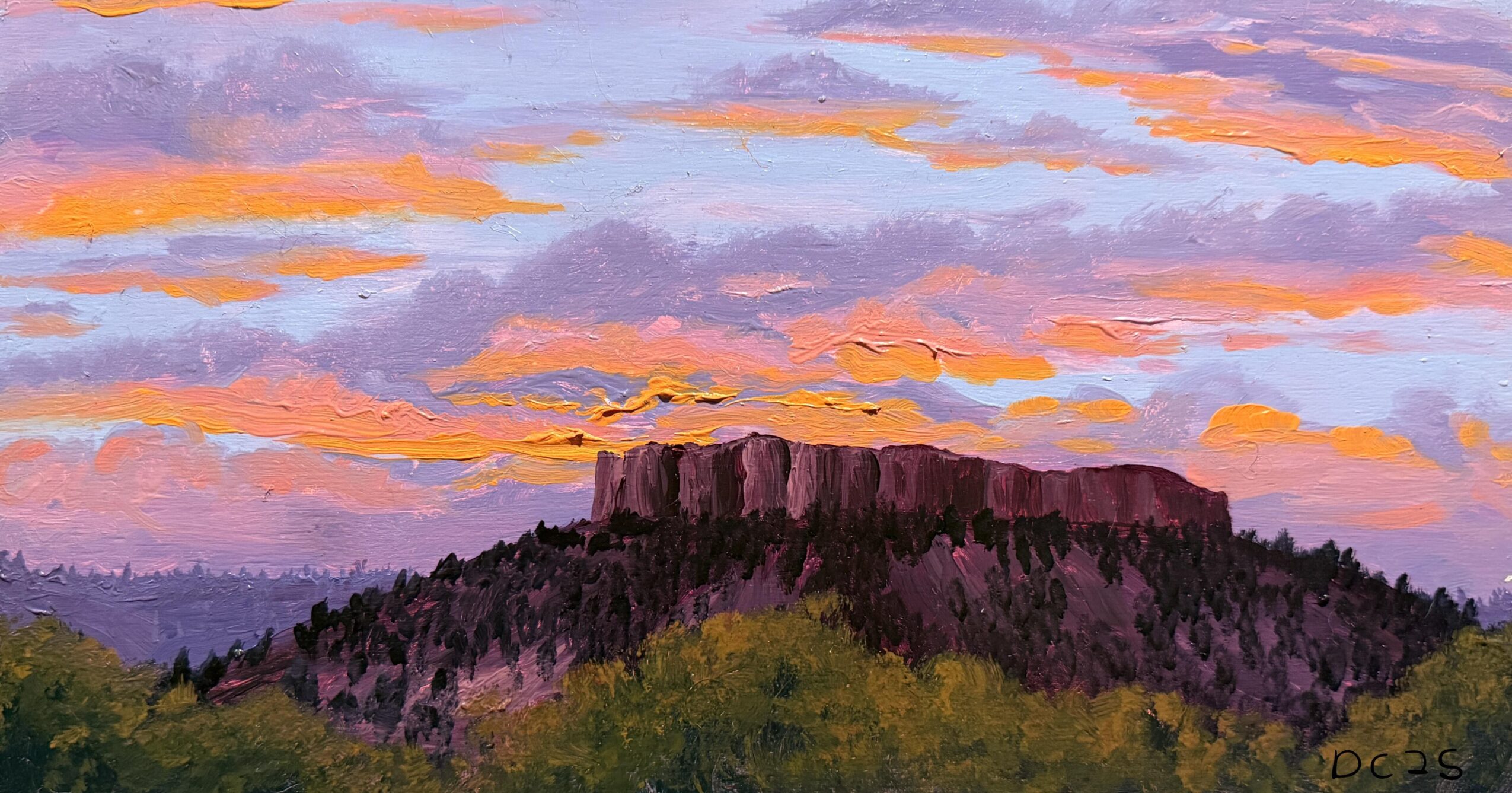Sunset sky with orange and purple clouds above a flat-topped mountain and green trees.