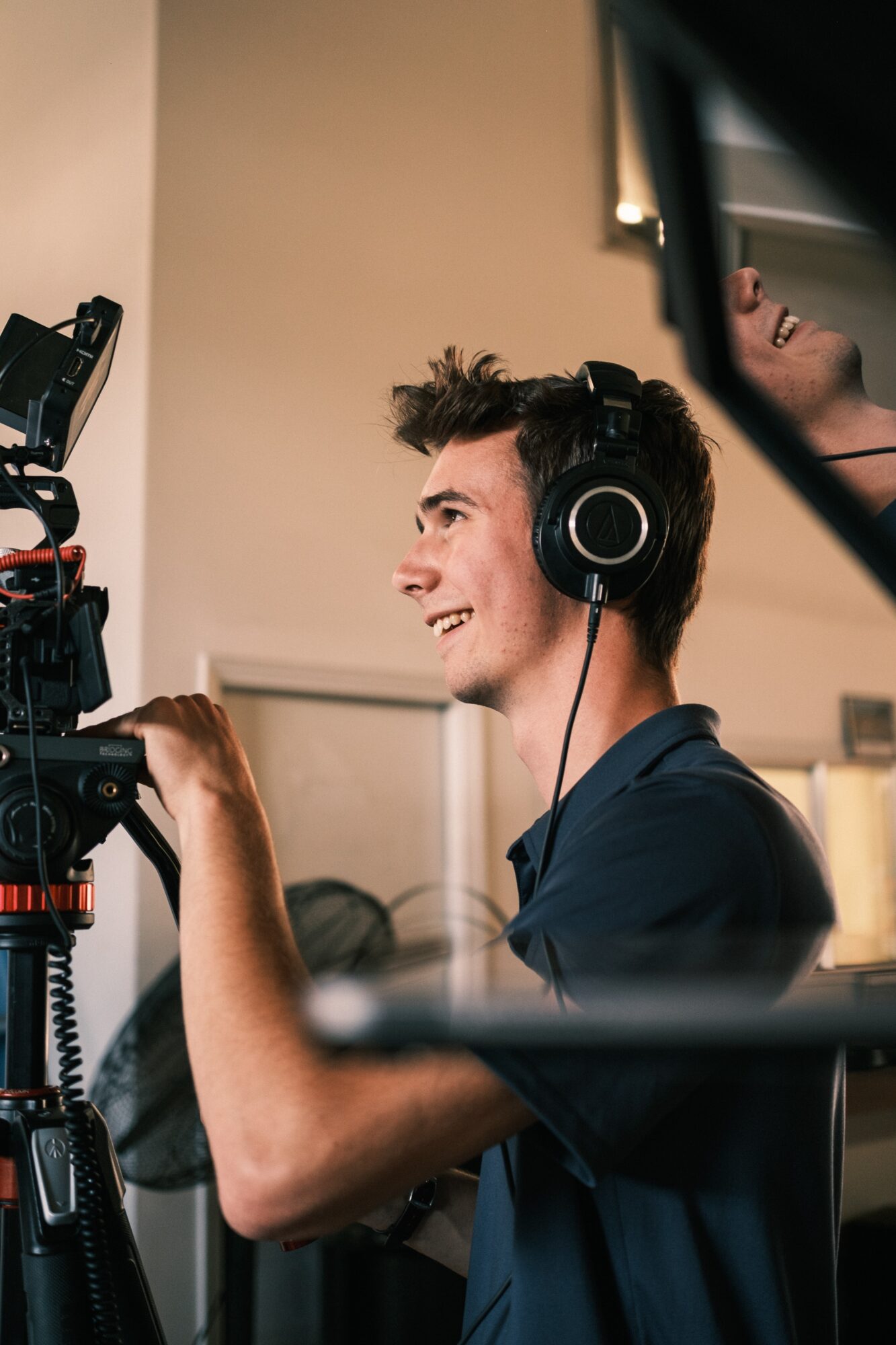 Young man with headphones operating camera equipment, smiling, in indoor setting.