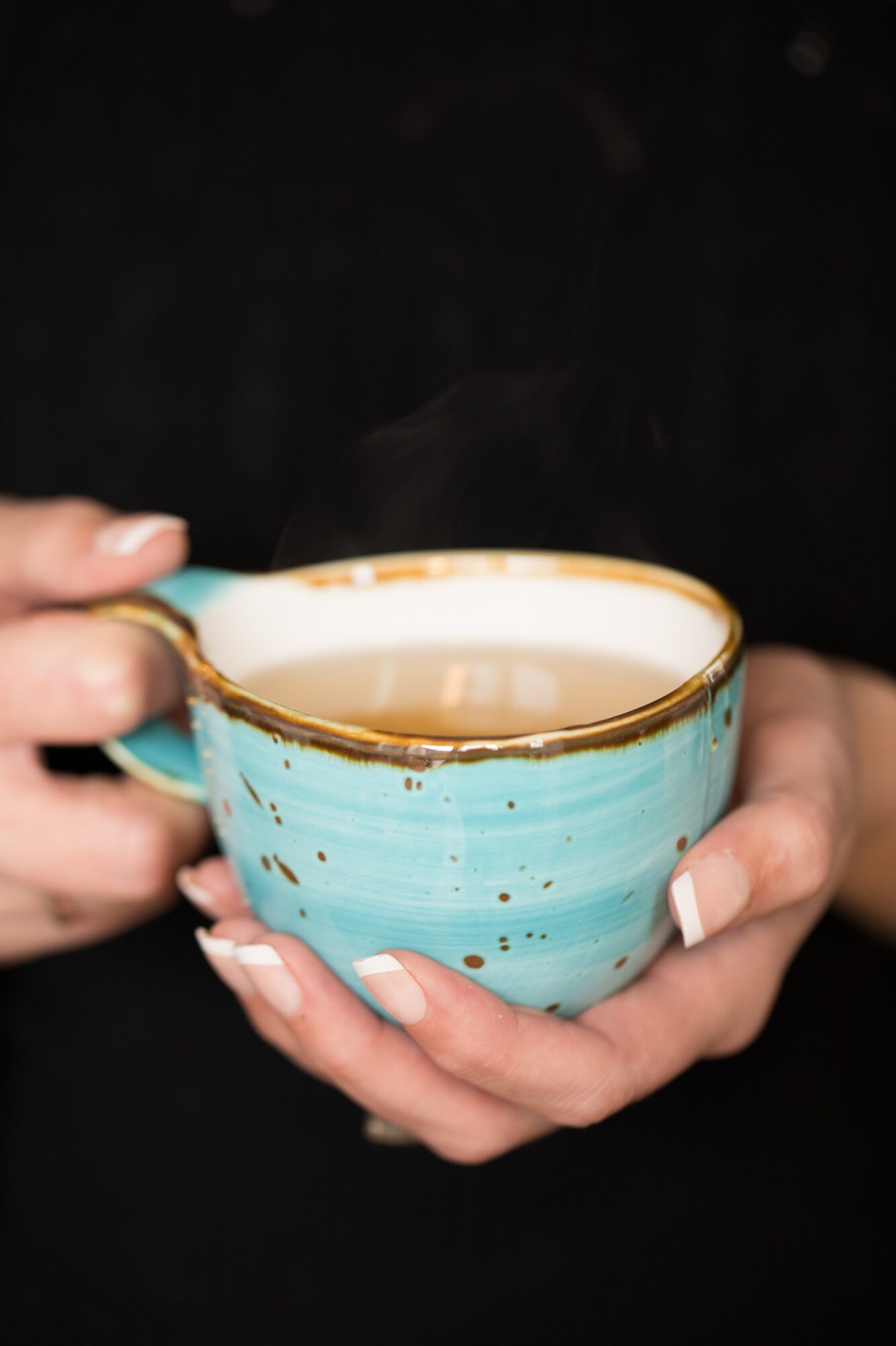 Person holds a blue ceramic cup filled with a hot beverage, with a dark background.
