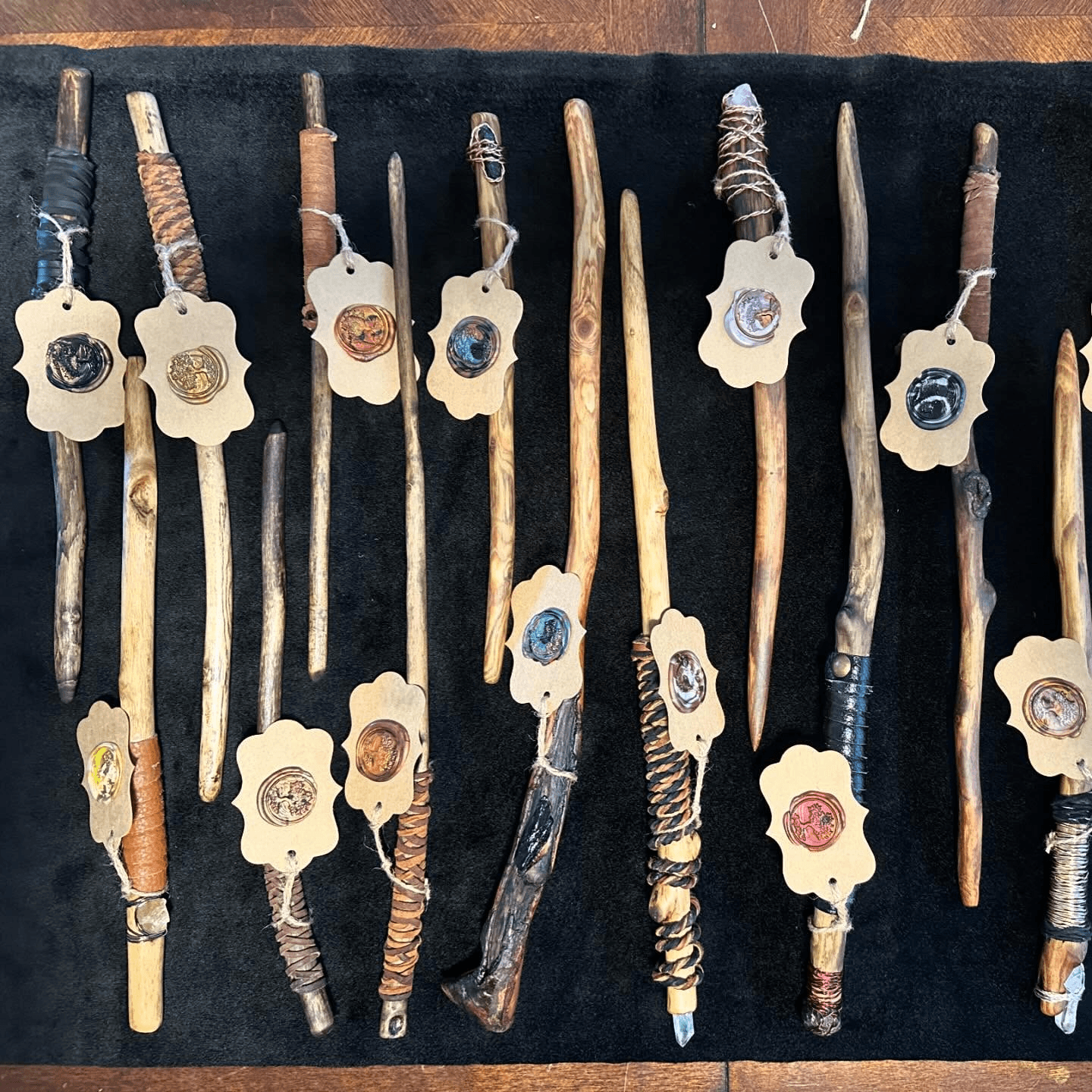 Collection of wooden wands with decorative tags, displayed on a black surface, varying in size and design.