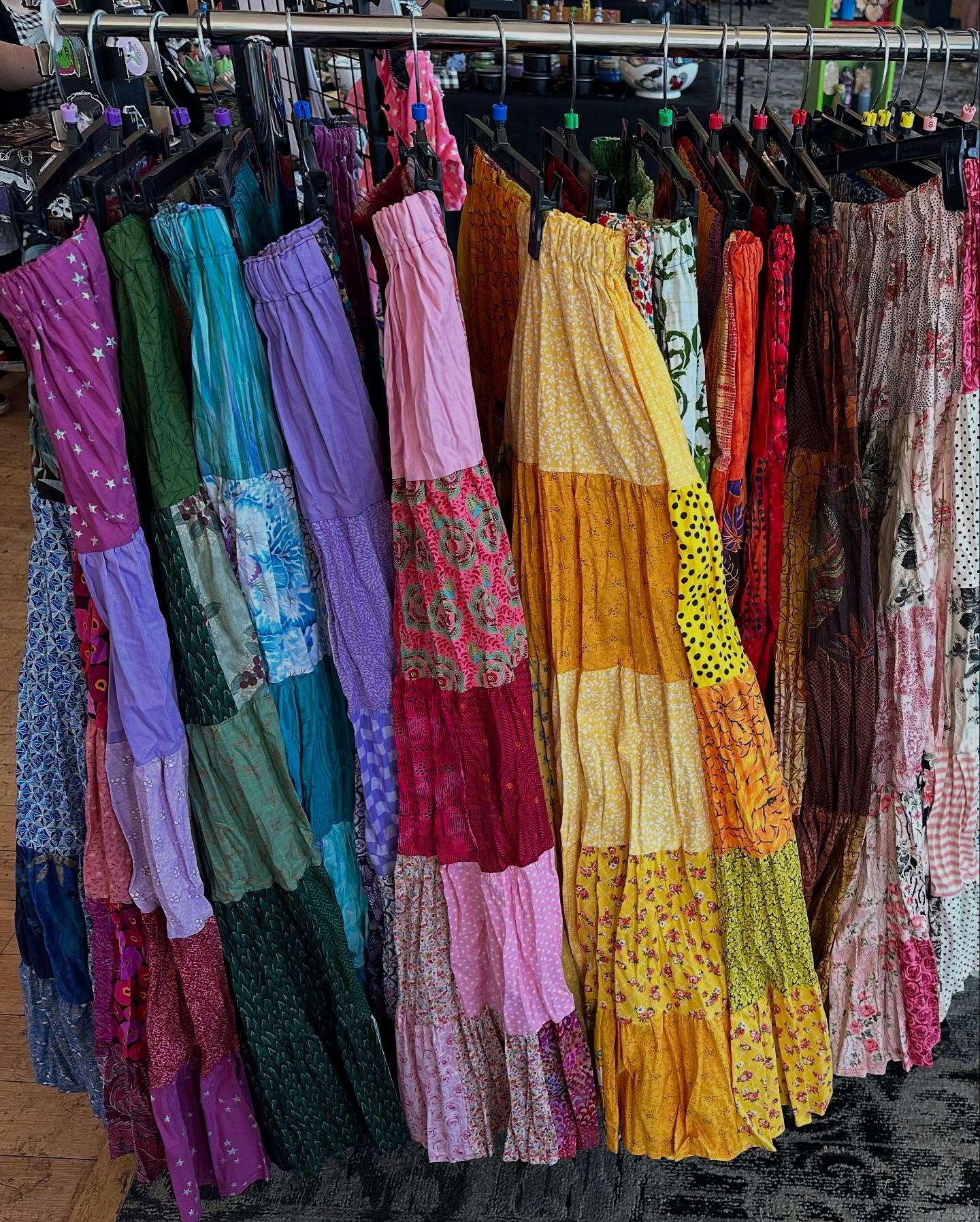 Colorful dresses hanging on a rack in a store, arranged by color from purple to pink and brown.