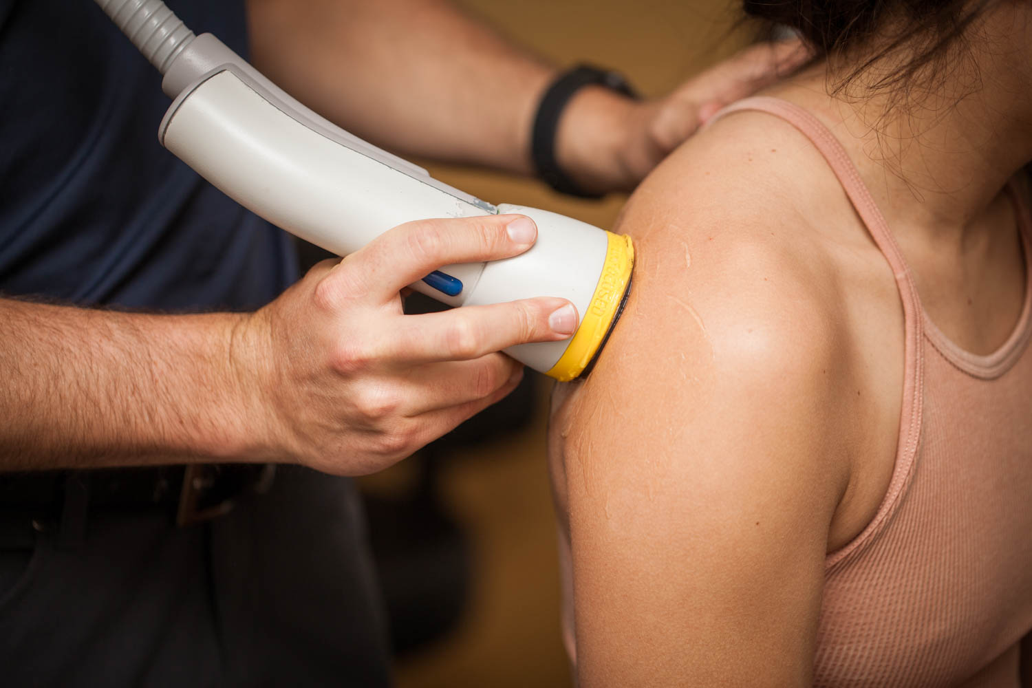Person receiving a shoulder ultrasound scan, with the device pressed against their shoulder, wearing a sleeveless top.