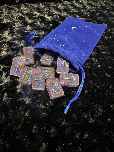 Small blue velvet bag with a moon and stars, partially open, spilling colorful rectangular objects onto a dark surface.