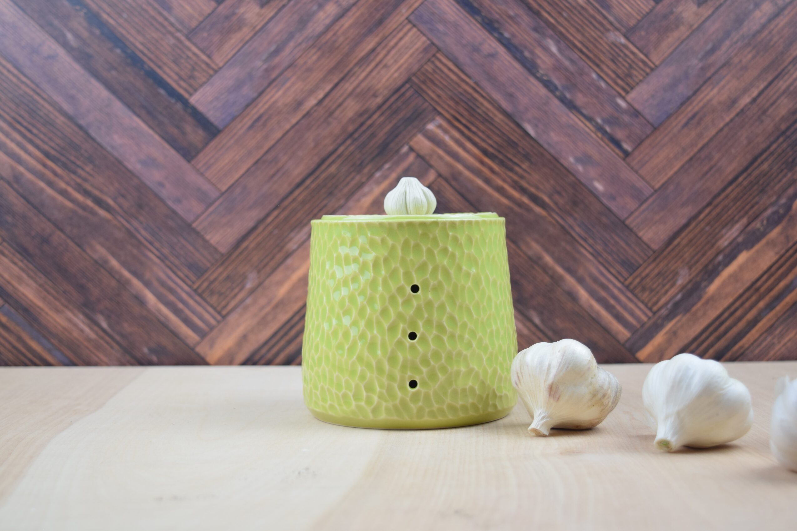 Green textured container with a small white object on top, surrounded by three white objects on a light surface, wooden background
