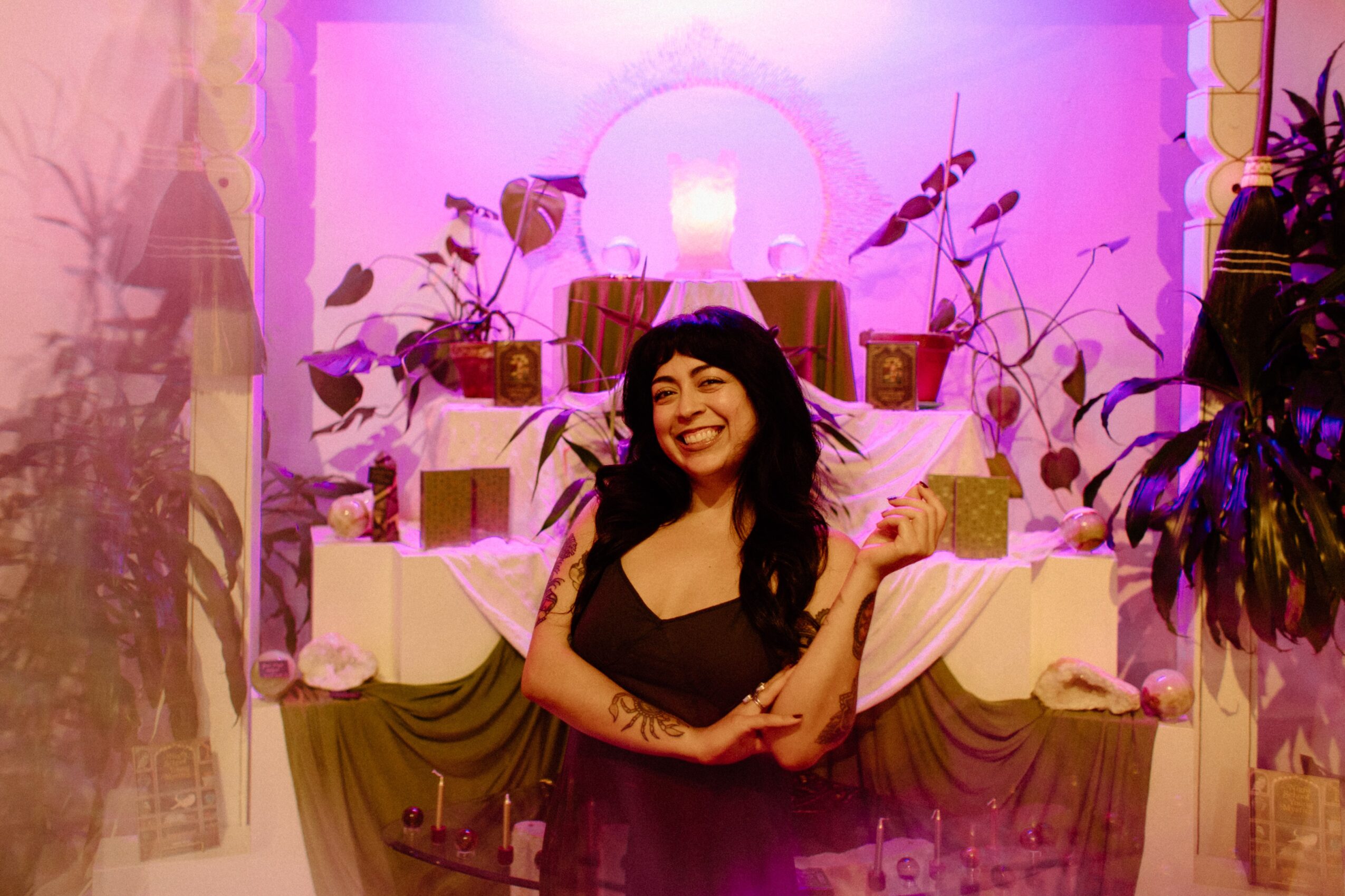 Smiling woman with dark hair in front of decorated backdrop with plants and pink lighting.