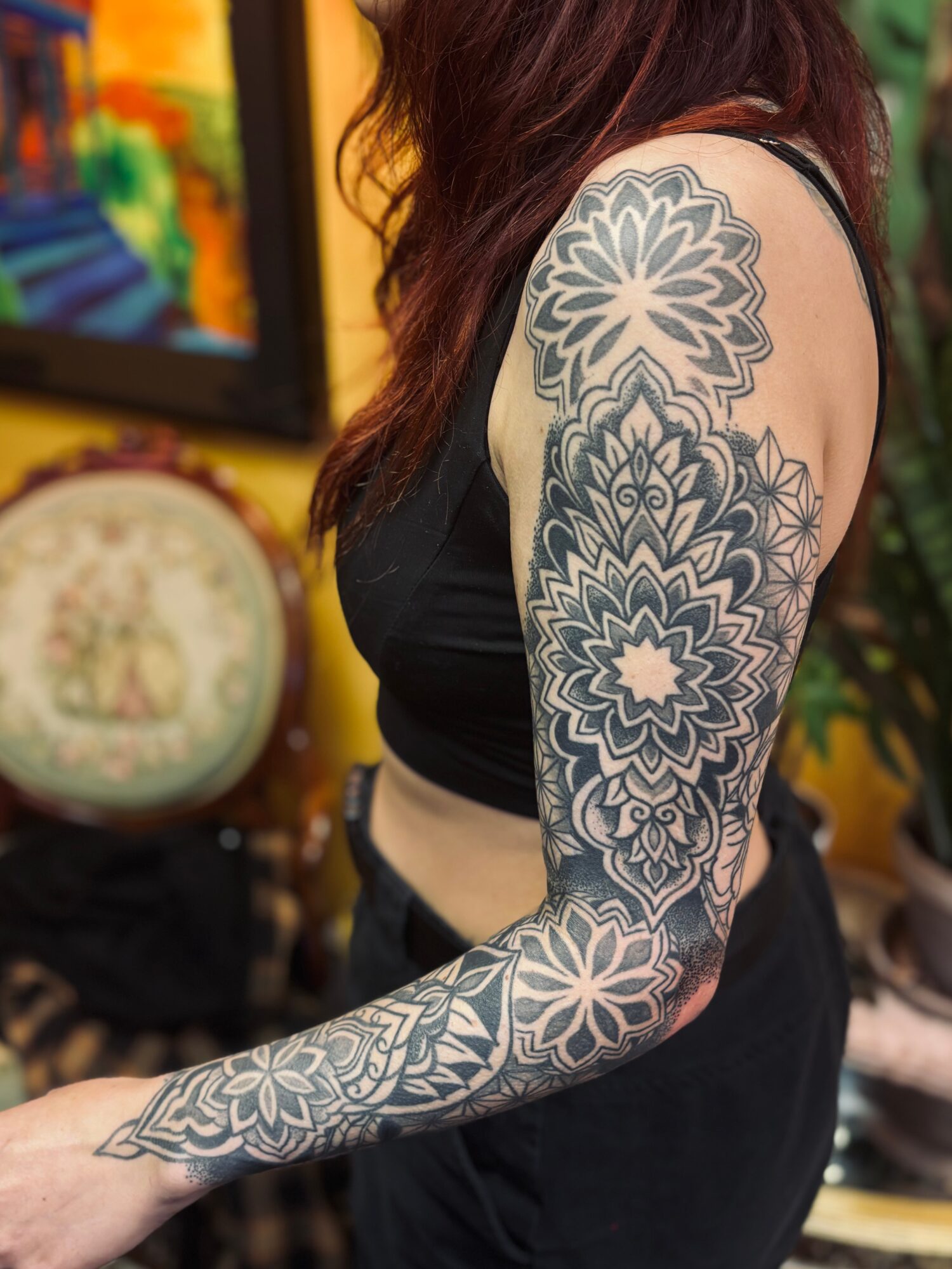 Woman with a large floral tattoo on her arm, wearing a black top, in a colorful indoor setting.