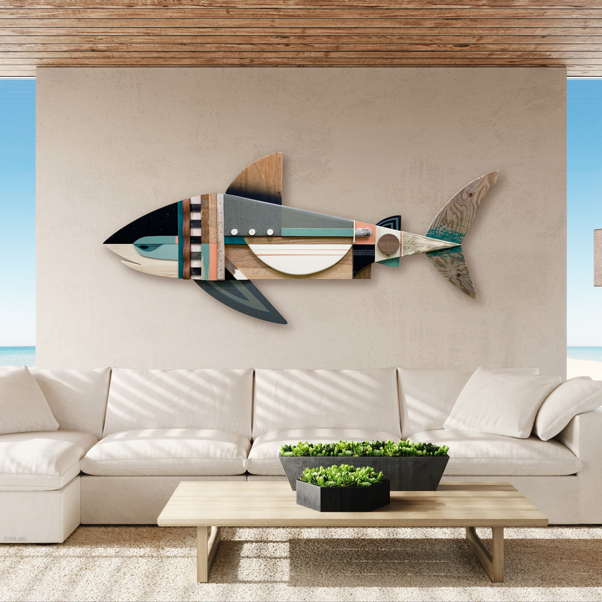 Decorative fish wall art with geometric shapes, mounted above a white sofa in a modern living room, with a wooden ceiling and ocean view.