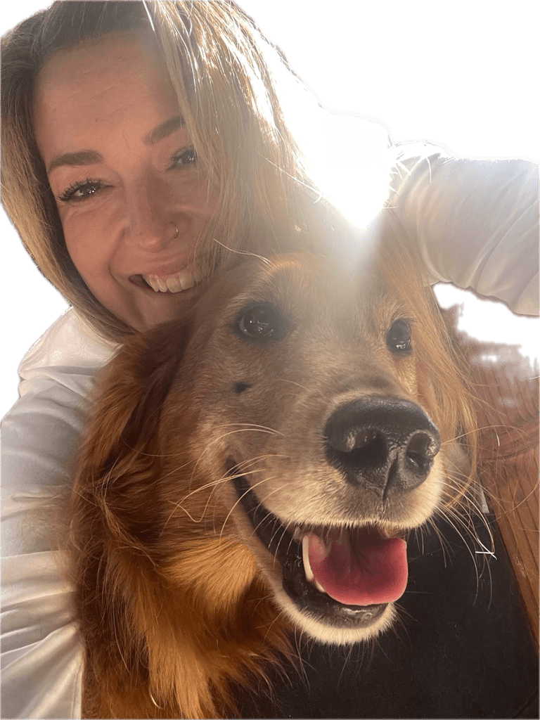 Person smiling with a golden retriever dog, both looking at the camera, bright light behind them.