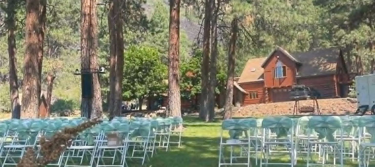 Outdoor event setup with chairs on grass, trees, and a house in the background.