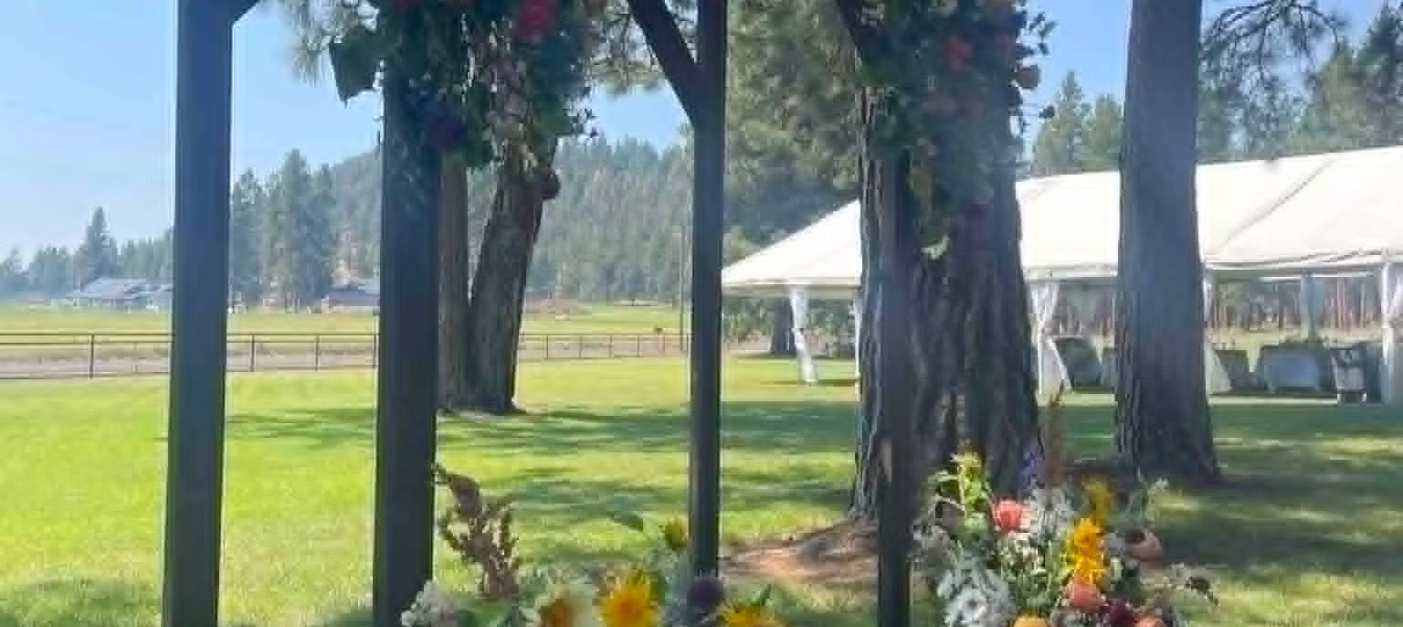 Outdoor scene with trees, a tent, and flowers, viewed through vertical bars, under a clear sky.
