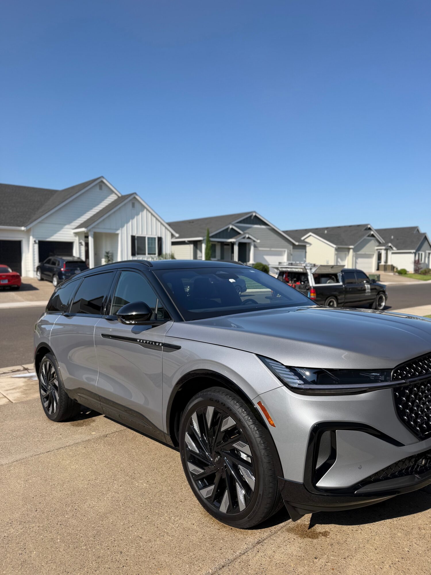 Silver SUV parked on driveway in front of suburban houses under clear blue sky.