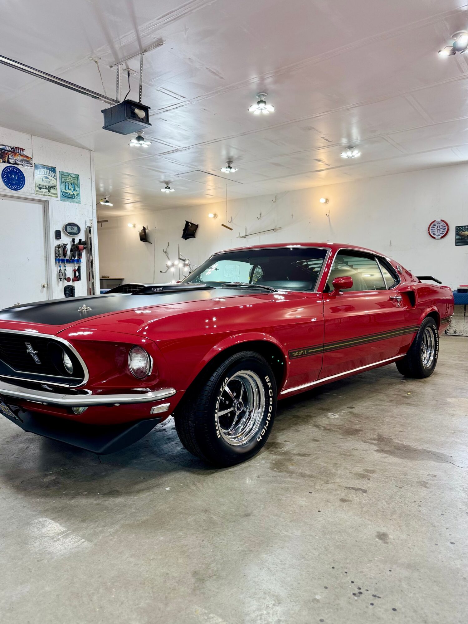 Red vintage car with chrome wheels parked indoors, white ceiling with lights, and garage tools on the wall.