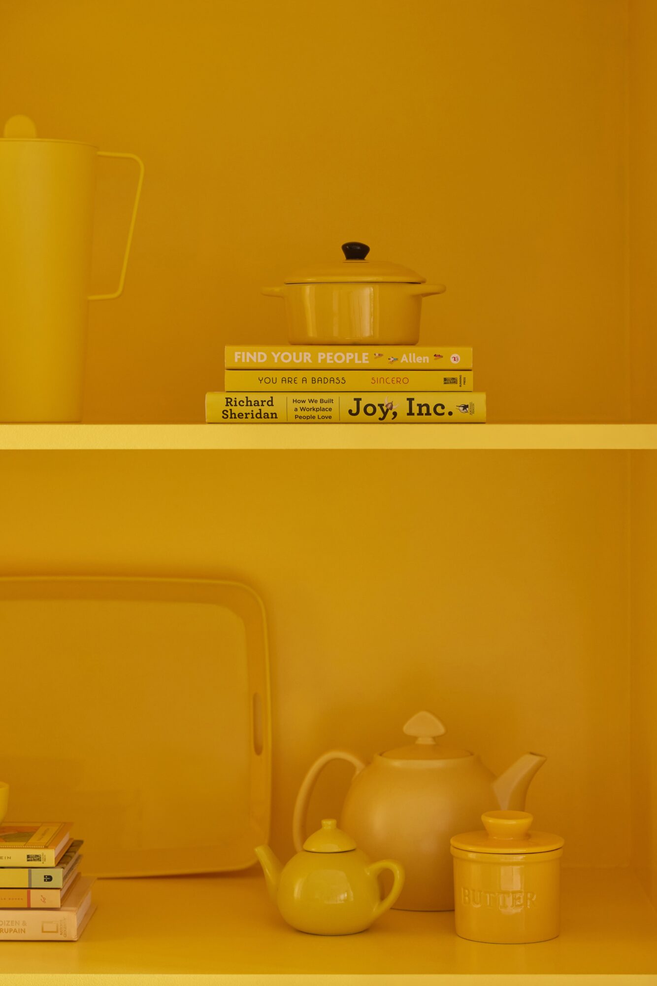 Shelf with books, teapot, and containers, against a yellow background.