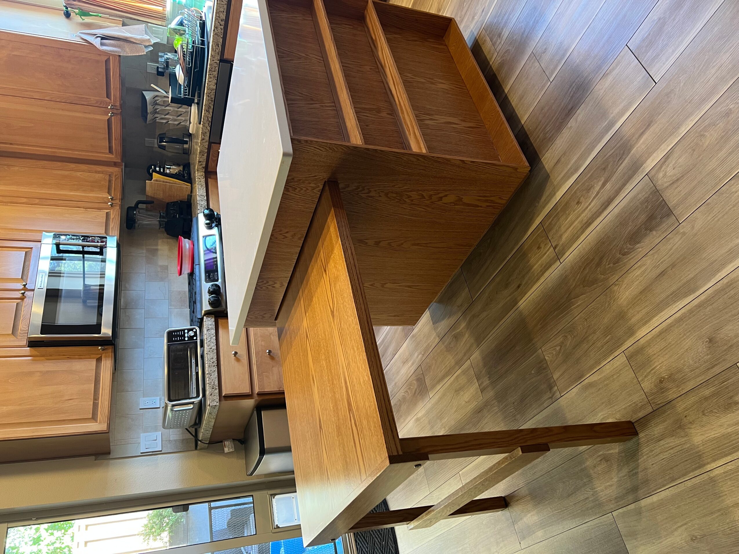 Wooden kitchen island with open shelves and a white countertop, adjacent to a wooden floor and kitchen appliances.