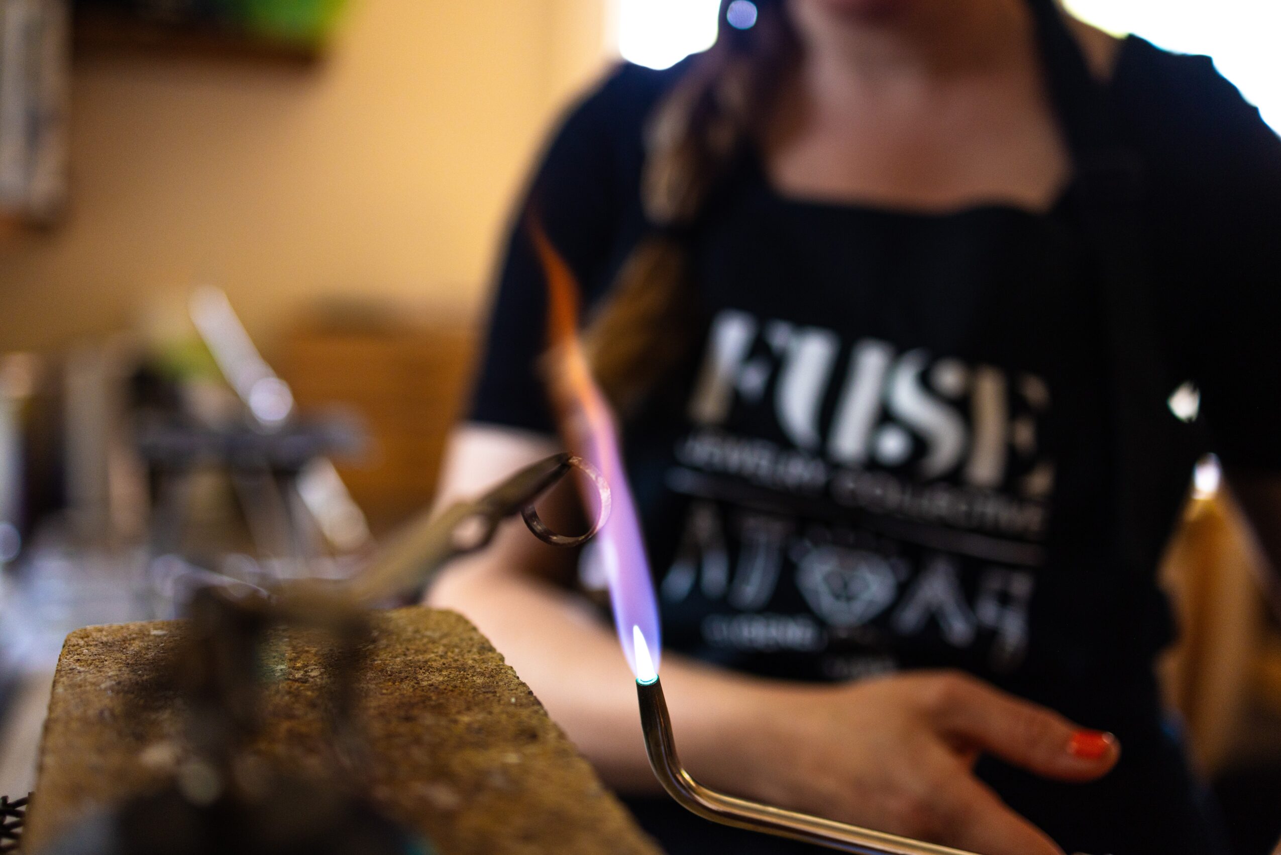 Person wearing a black shirt and apron, working with a tool on a surface, in a room with warm lighting.