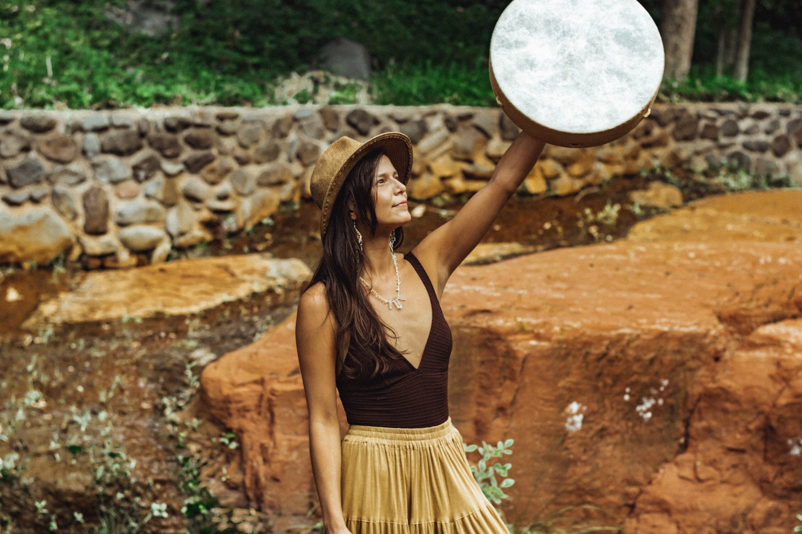 Woman holding a large circular object outdoors with rocks and greenery in background.
