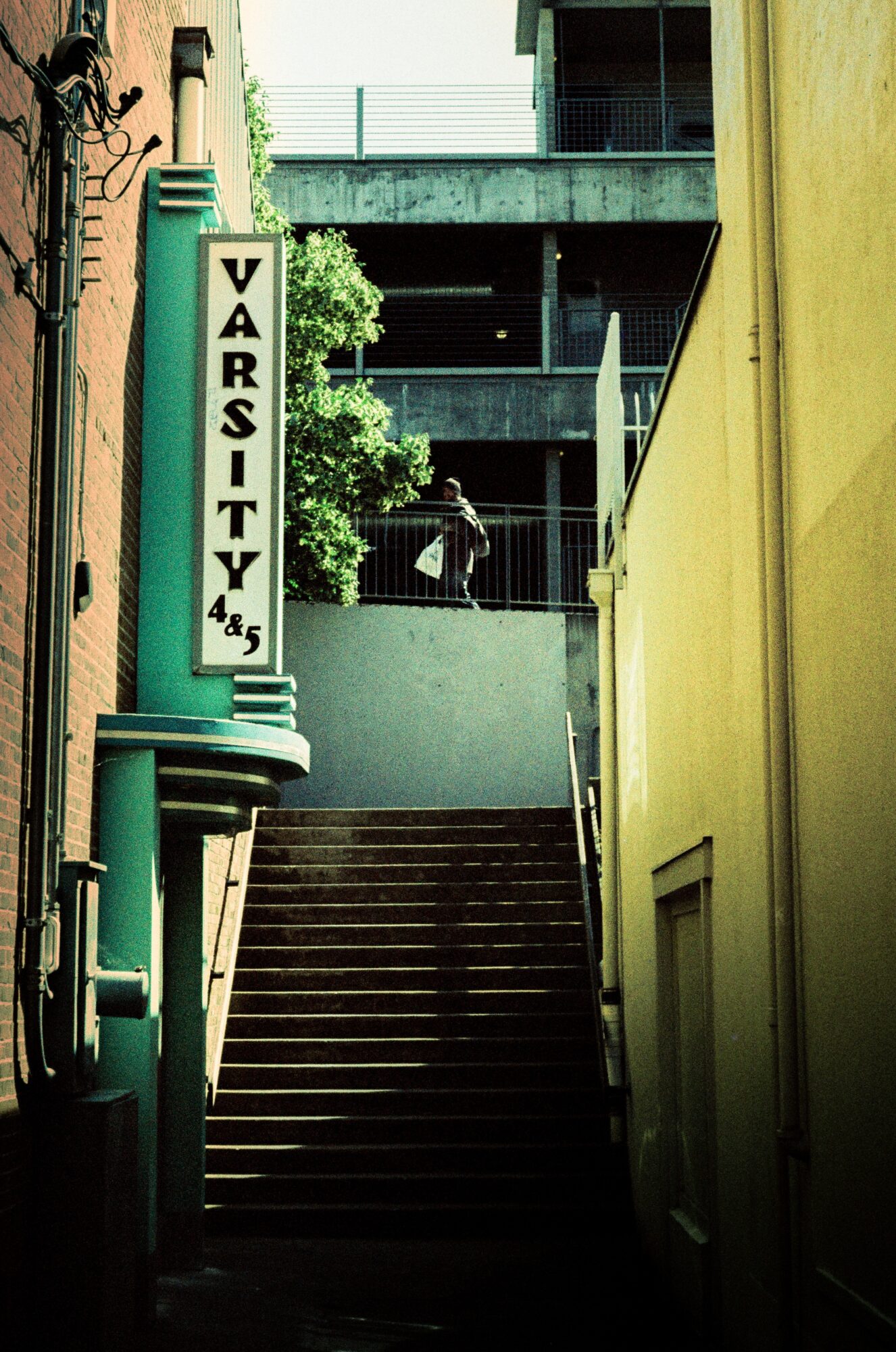 Staircase between buildings with a person standing at the top, green and yellow walls, and a sign reading 'VARSITY 45'.
