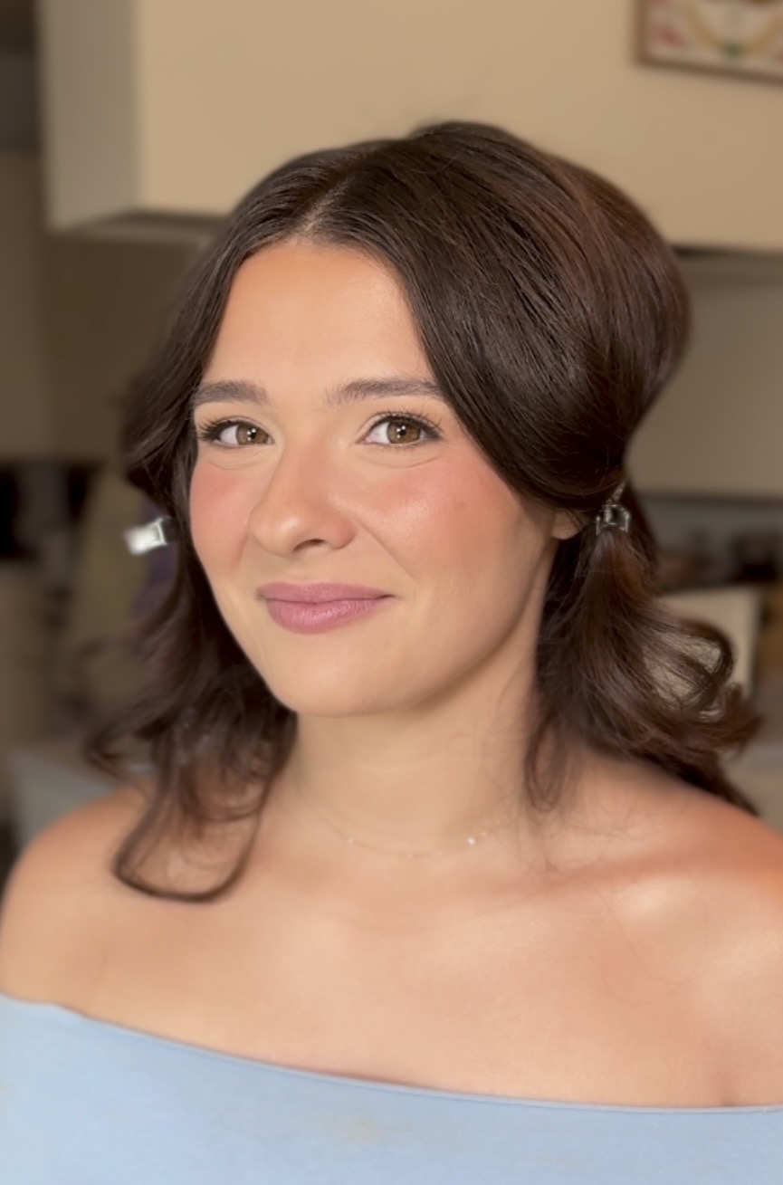 Woman with shoulder-length brown hair, smiling, wearing a light blue top, in an indoor setting.