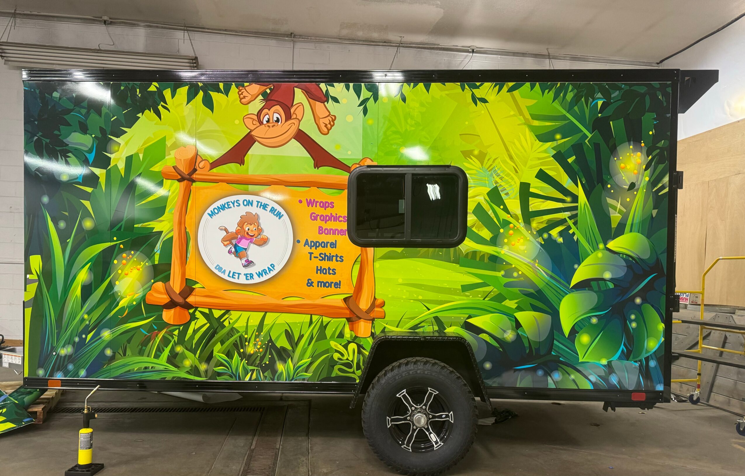 Mobile trailer with jungle-themed design, featuring a cartoon monkey, lush green foliage, and a sign about a children's event.