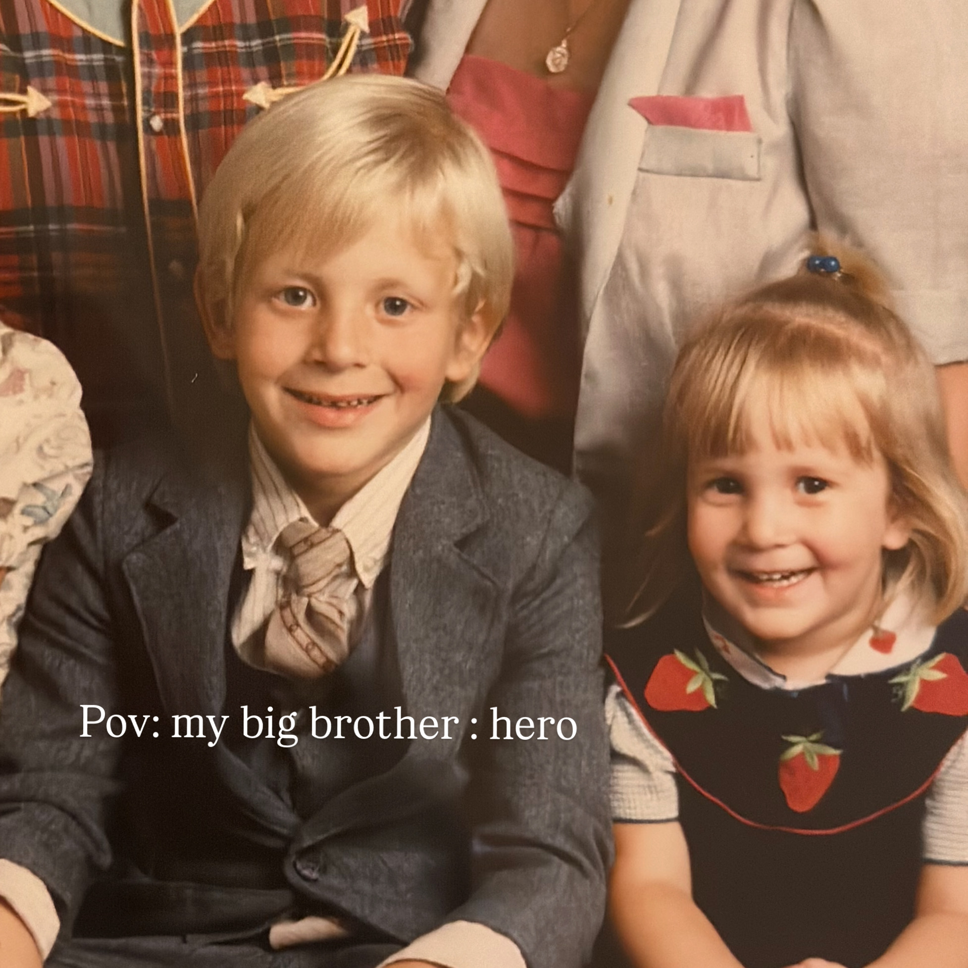 Two children smiling, a boy with blond hair in a suit and a girl with light brown hair in a dress, in a group photo.