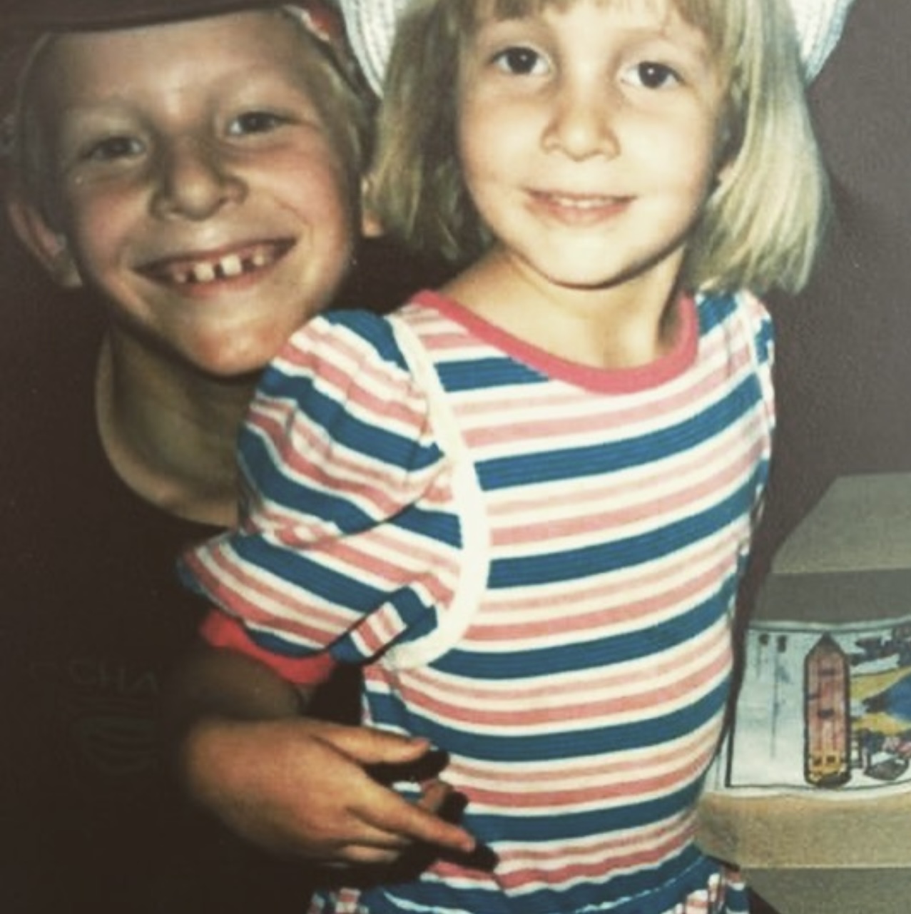 Two children, a boy and a girl, smiling and standing close together, girl wearing a striped shirt, boy with missing teeth.