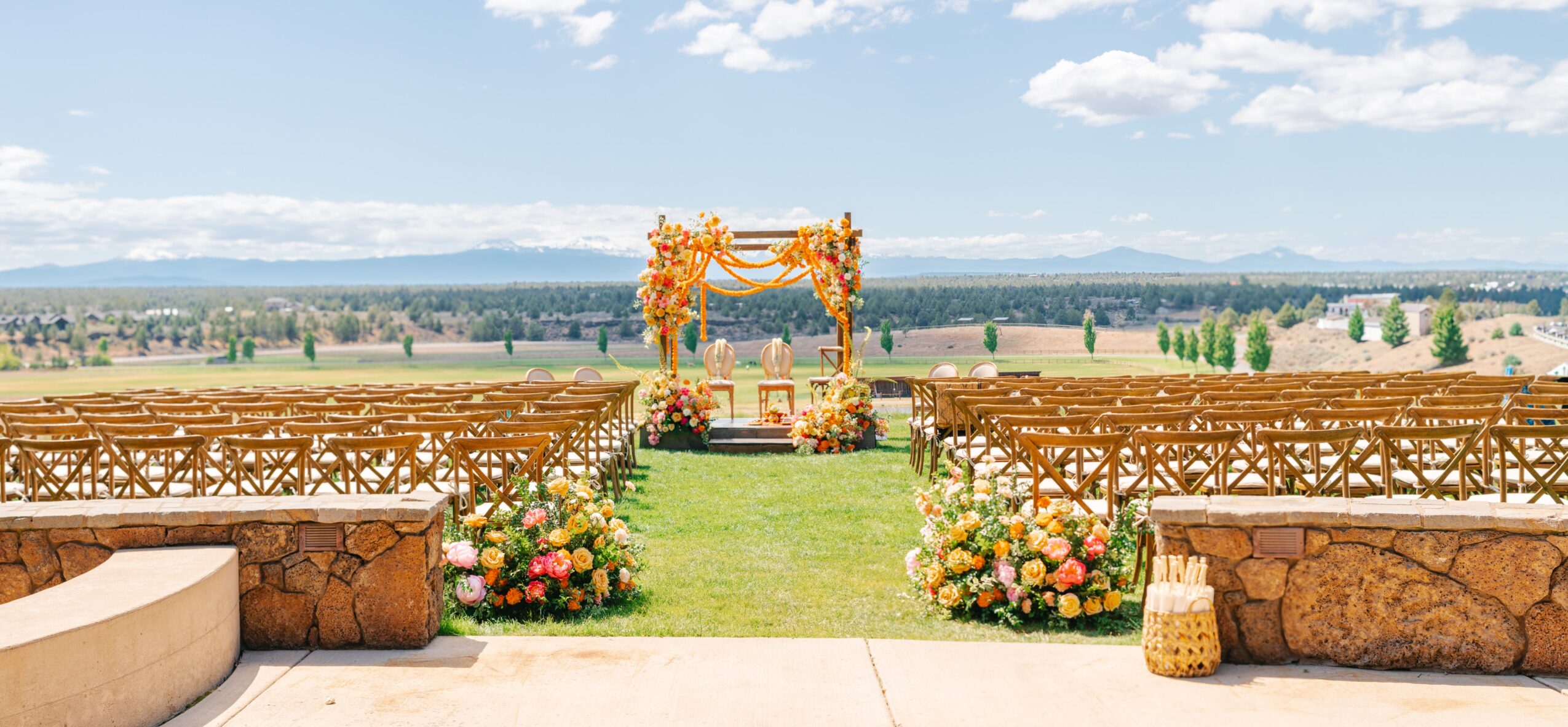Outdoor wedding setup with floral arch, rows of chairs, and a scenic landscape background.