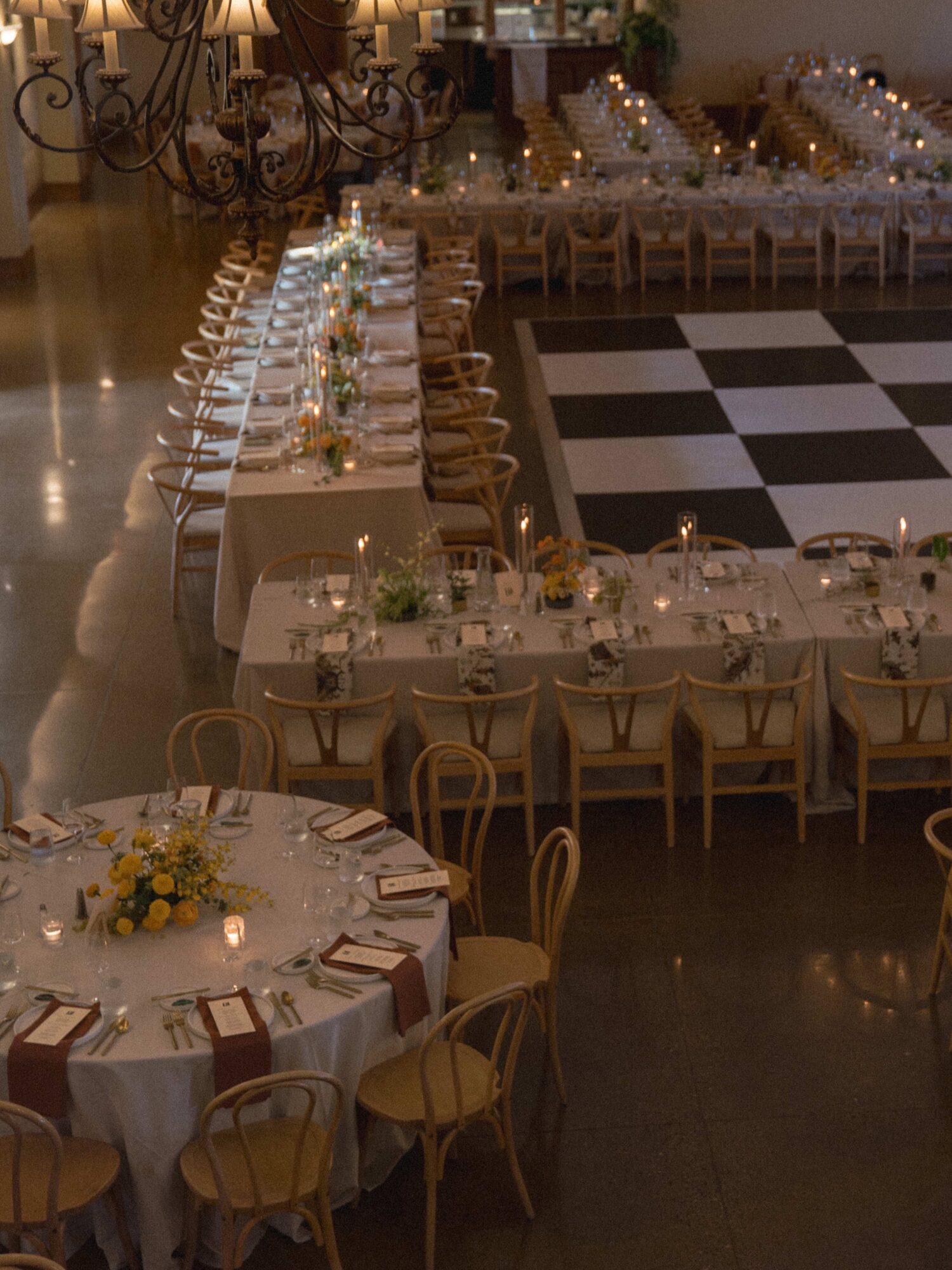 Elegant banquet hall with round and rectangular tables decorated with flowers and candles, set for a formal event.