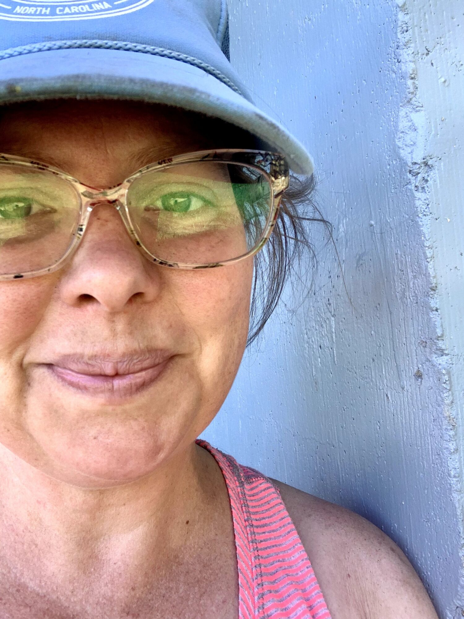 Close-up of a woman wearing glasses and a blue cap, smiling, with a blue wall background.