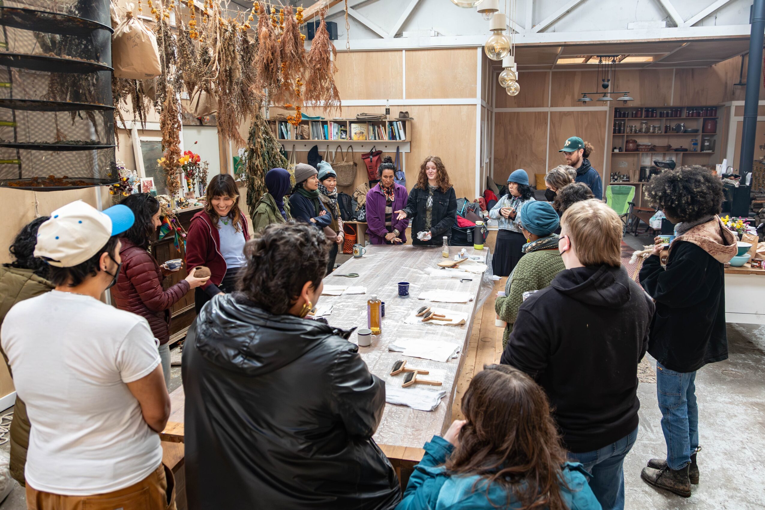 Group of people gathered around a long table in a rustic indoor space, engaging in a workshop or activity.