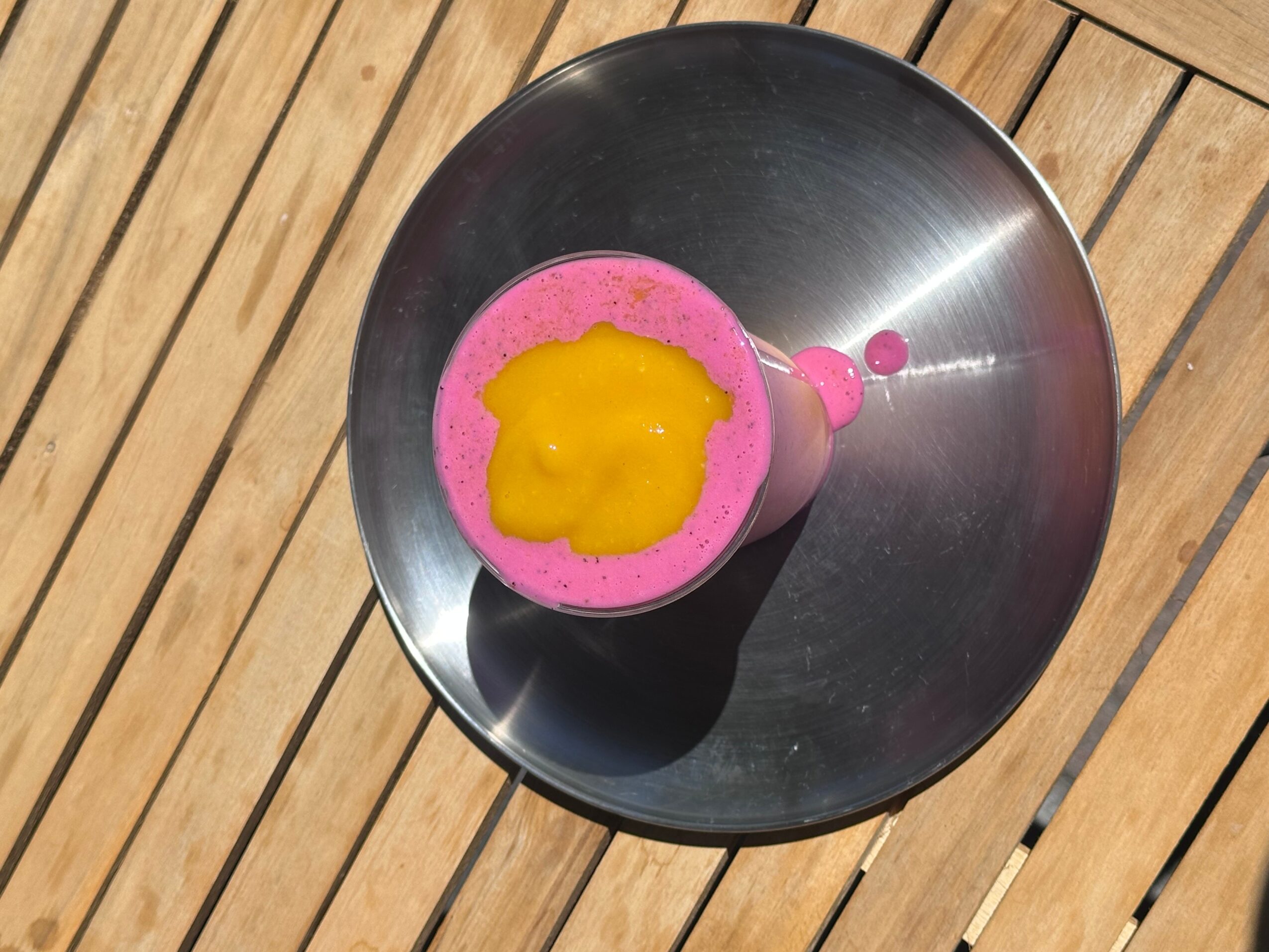 Pink foam with yellow liquid on top in a metal bowl on wooden surface.