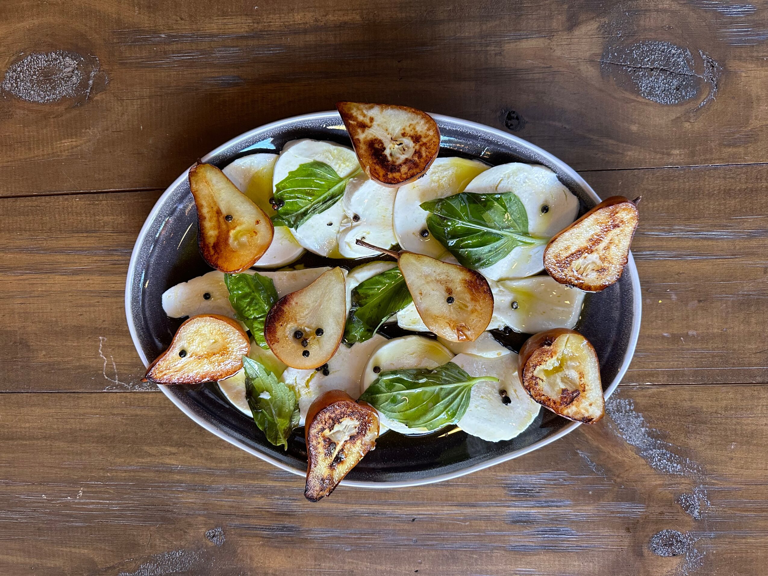 Bowl of mozzarella cheese, basil leaves, and toasted bread slices on a wooden surface.