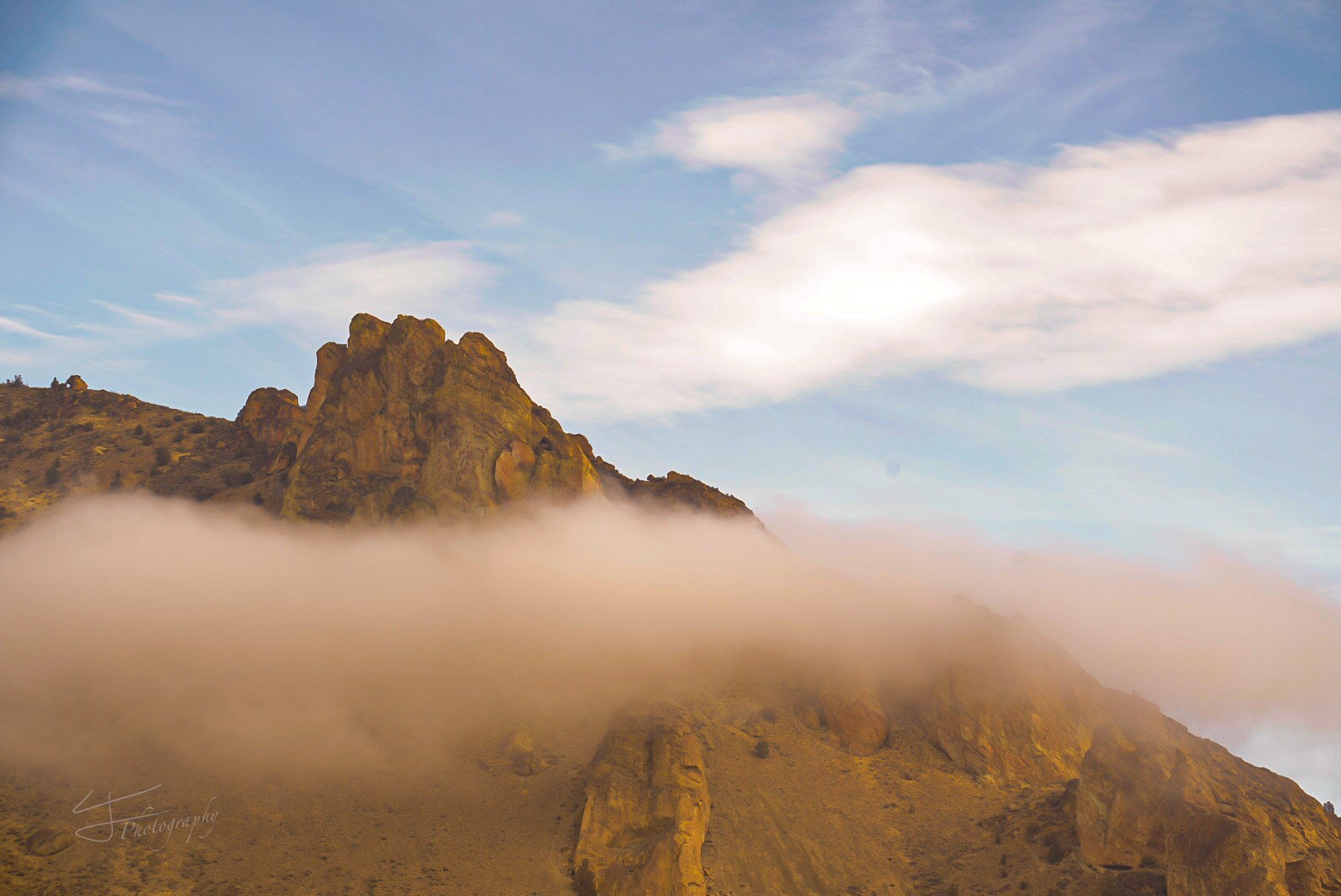 Mountain peak with clouds and sky, fog covering lower part of mountain, blue sky with clouds above.