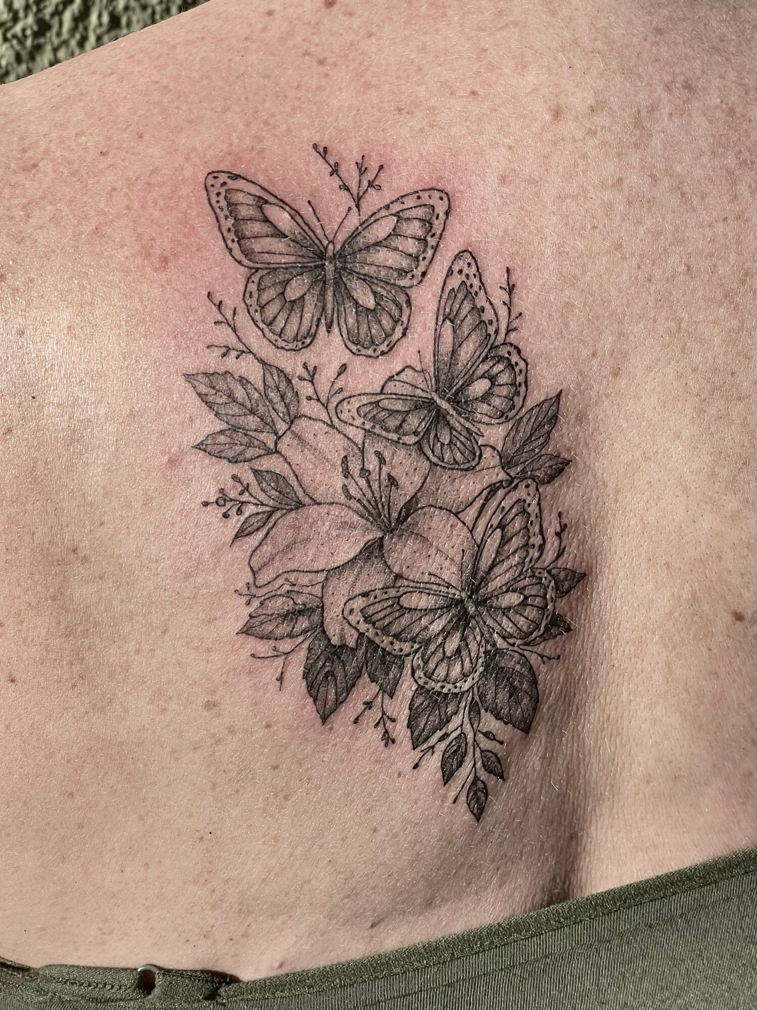 A tattoo of butterflies and flowers on skin, detailed line work, black ink, natural skin tone background.