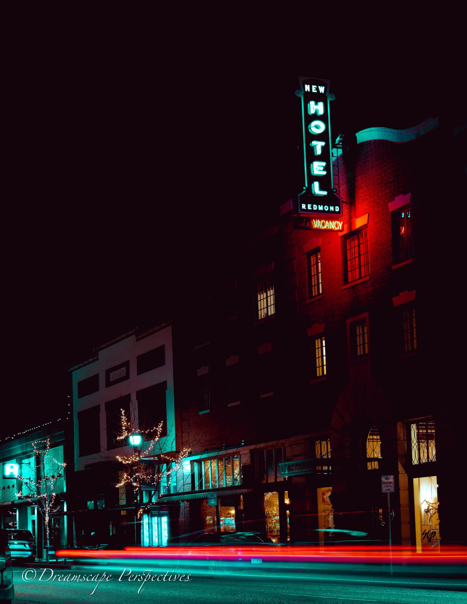 Night view of a building with a neon hotel sign, illuminated windows, and light trails from moving vehicles.