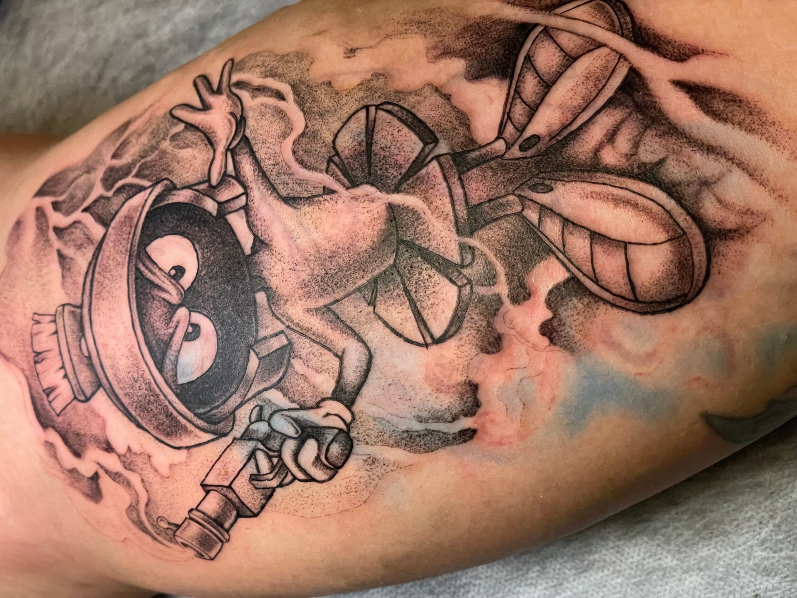 Tattoo of a cartoon-style bomb with a lit fuse, a hand, and a clock, on skin.