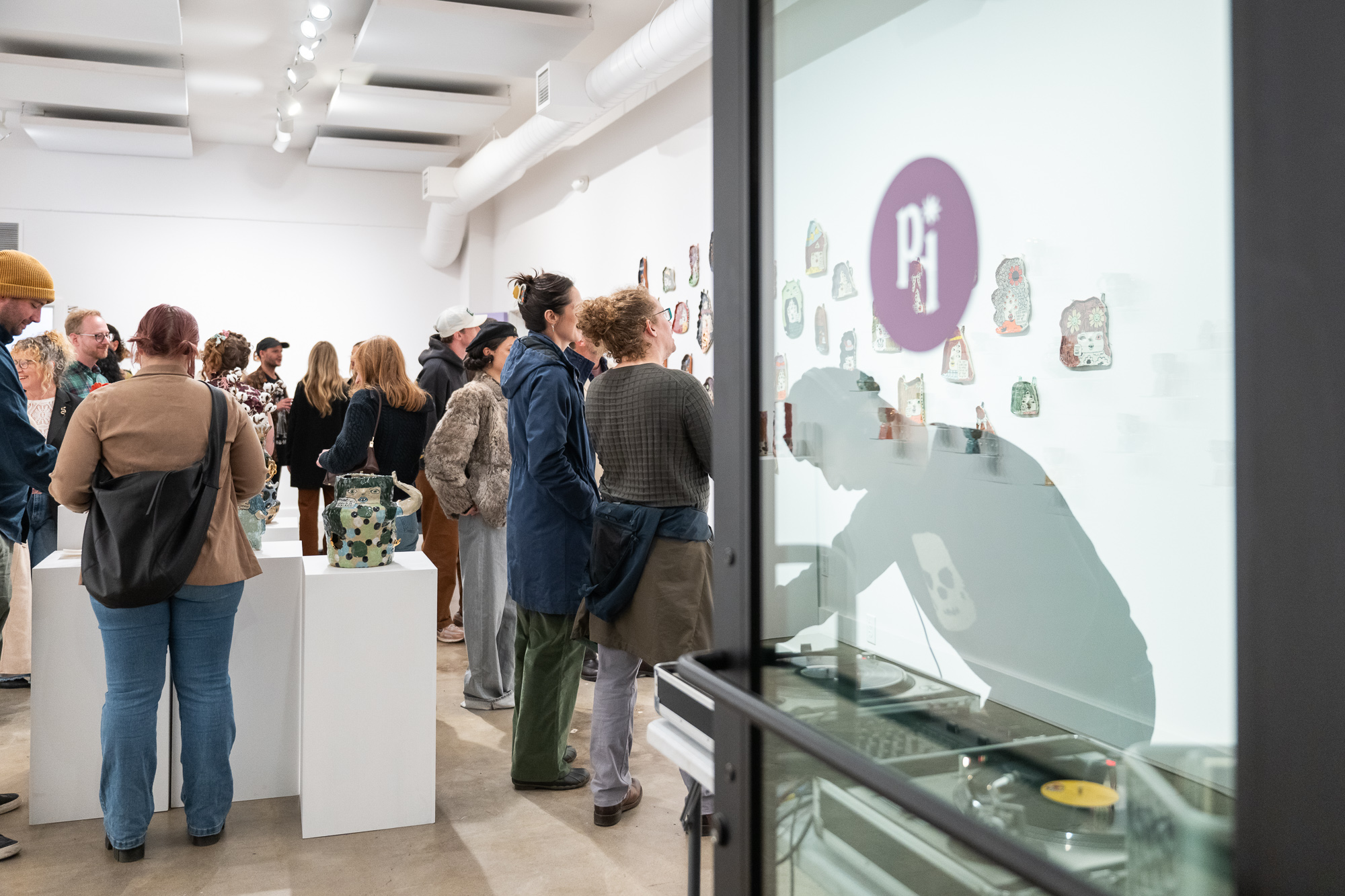 People gather in an art gallery, viewing artwork and displays on white walls and pedestals.