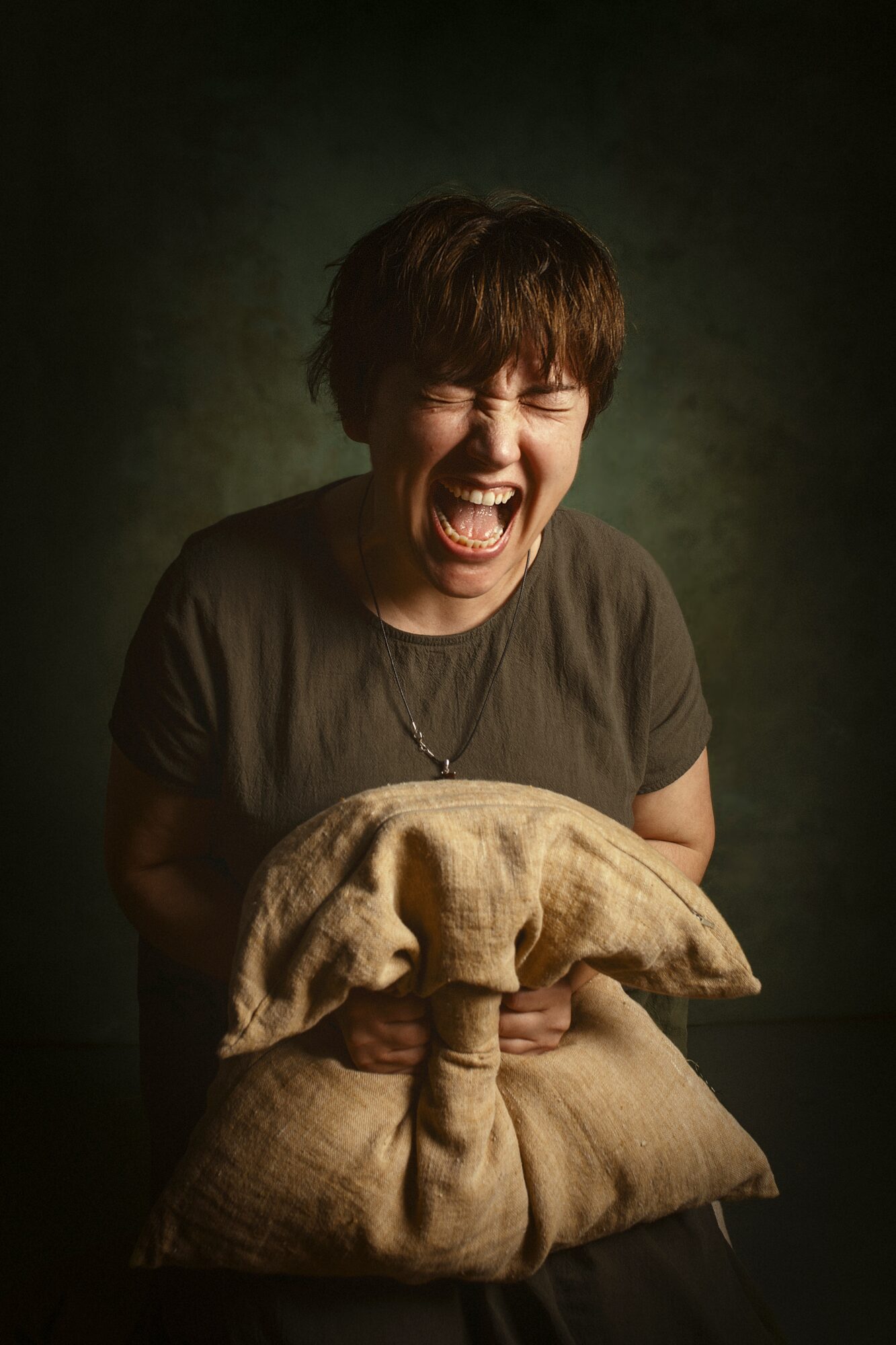 Person with short hair laughing, holding a cloth bundle, dark background, expressive emotion.