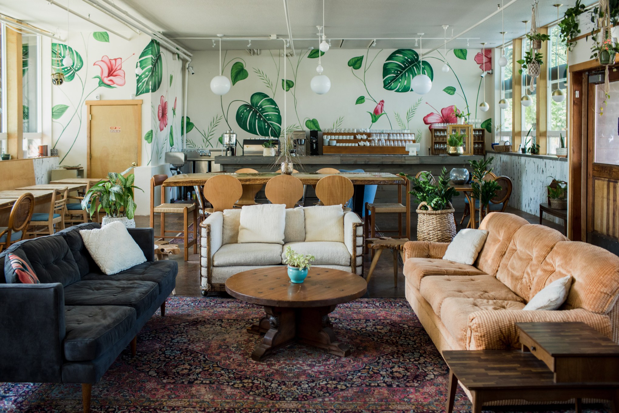 Living room with tropical leaf wallpaper, sofas, a piano, and plants, illuminated by natural light from windows.