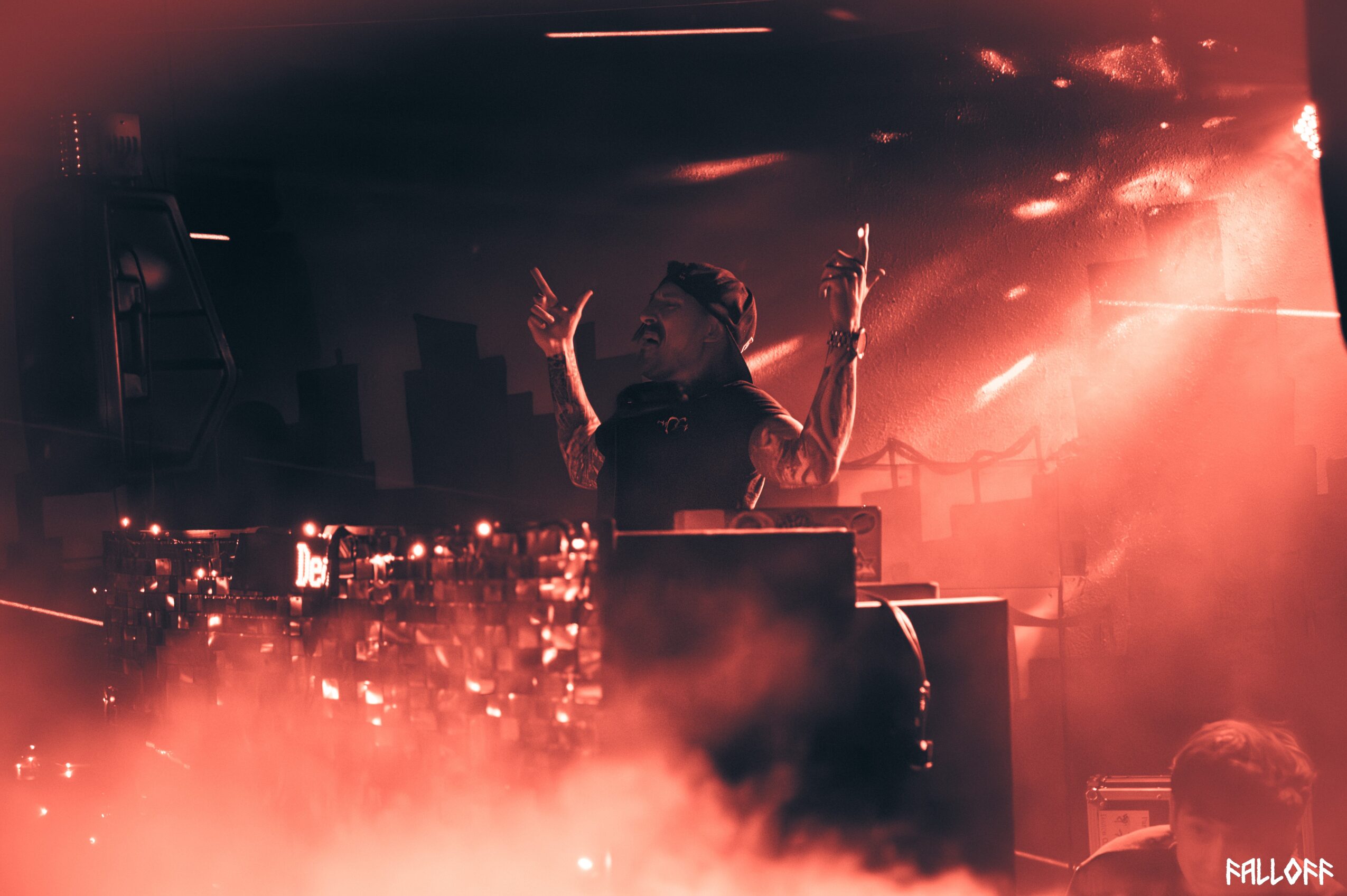 Person performing on stage with arms raised, surrounded by stage lights and fog, in a concert setting.