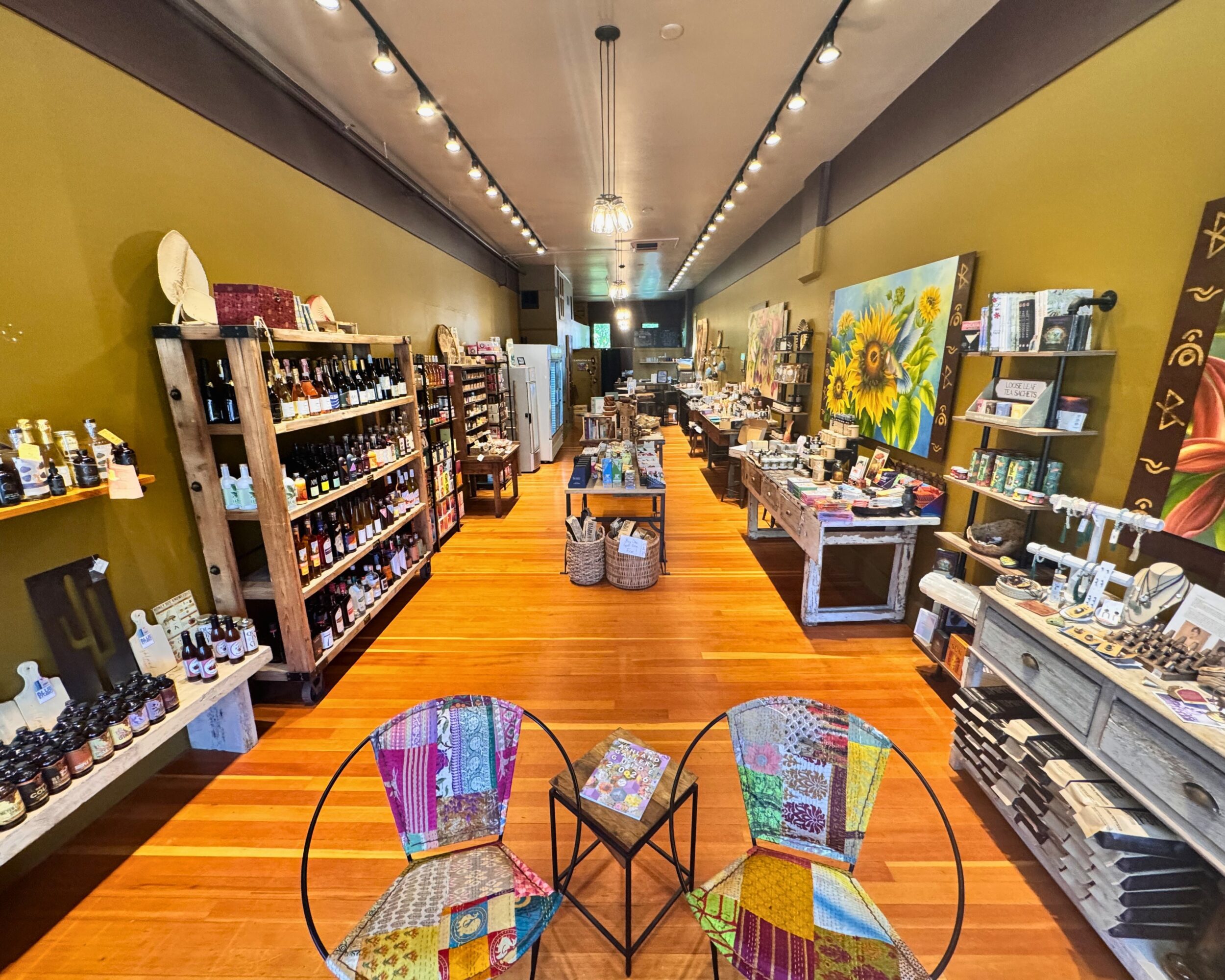 Interior of a store with shelves of products, colorful chairs, and artwork on the walls, viewed from the entrance.