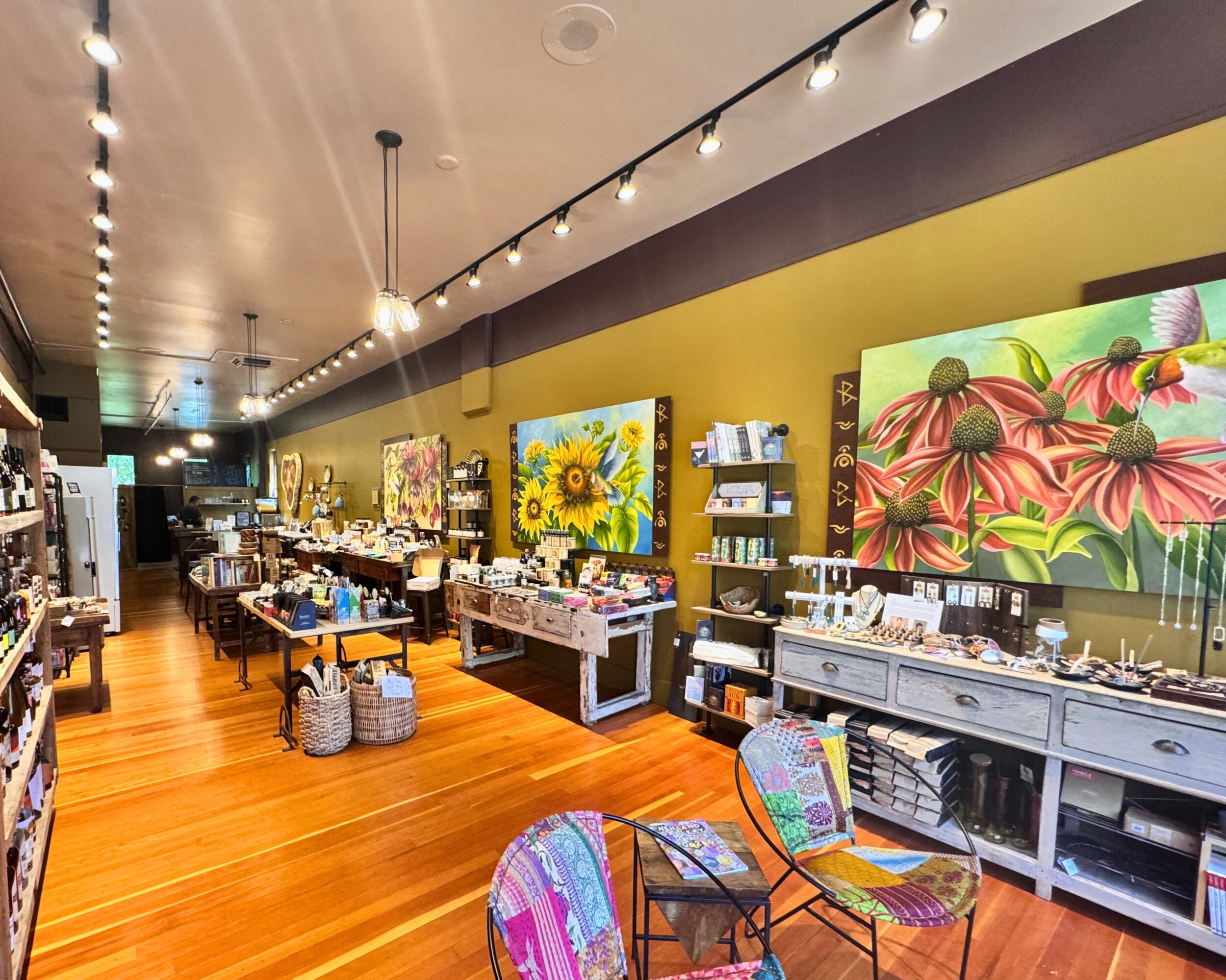 Interior of an art gallery with colorful paintings, tables, and chairs, and wooden flooring.