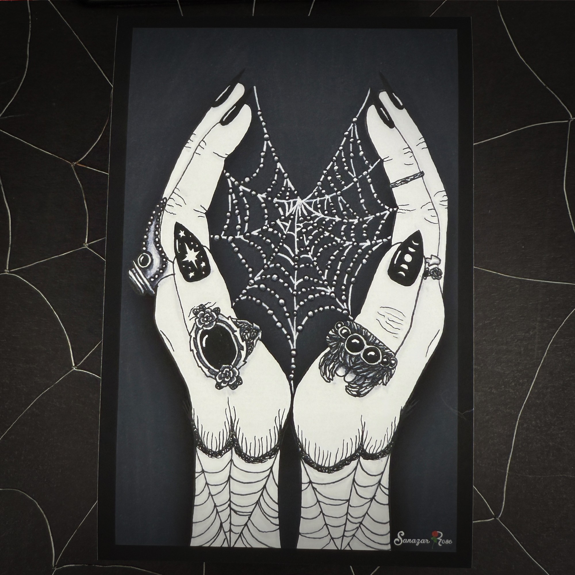 Two hands with rings and painted nails hold a spider web, with spider and web details, on a dark background.