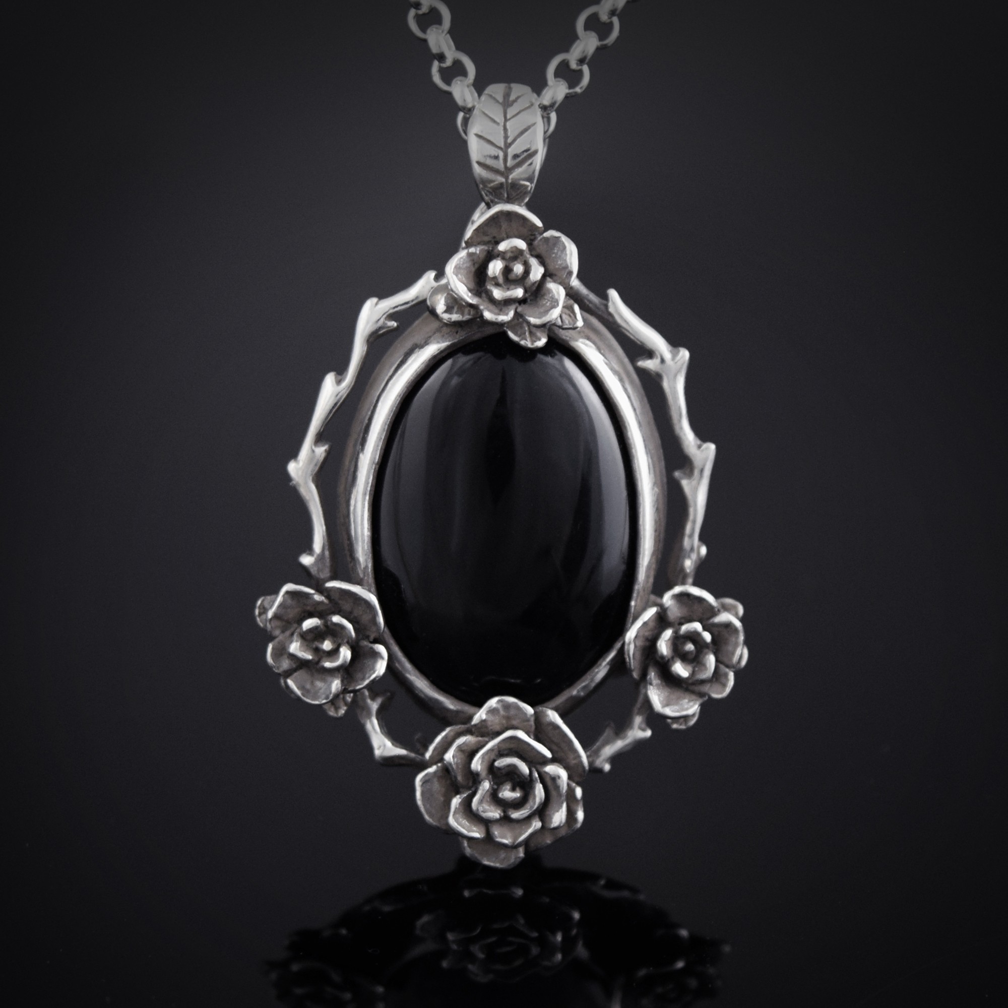 Silver necklace with a large black oval gemstone surrounded by detailed floral designs, hanging against a dark background.
