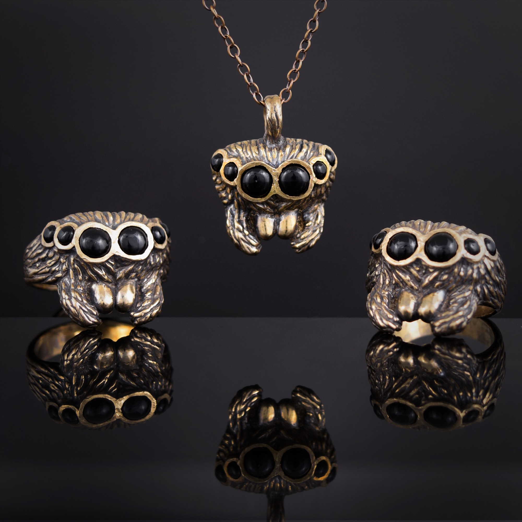 Set of jewelry including a necklace and two rings, all featuring animal designs with black gemstone eyes, displayed on a reflective surface.