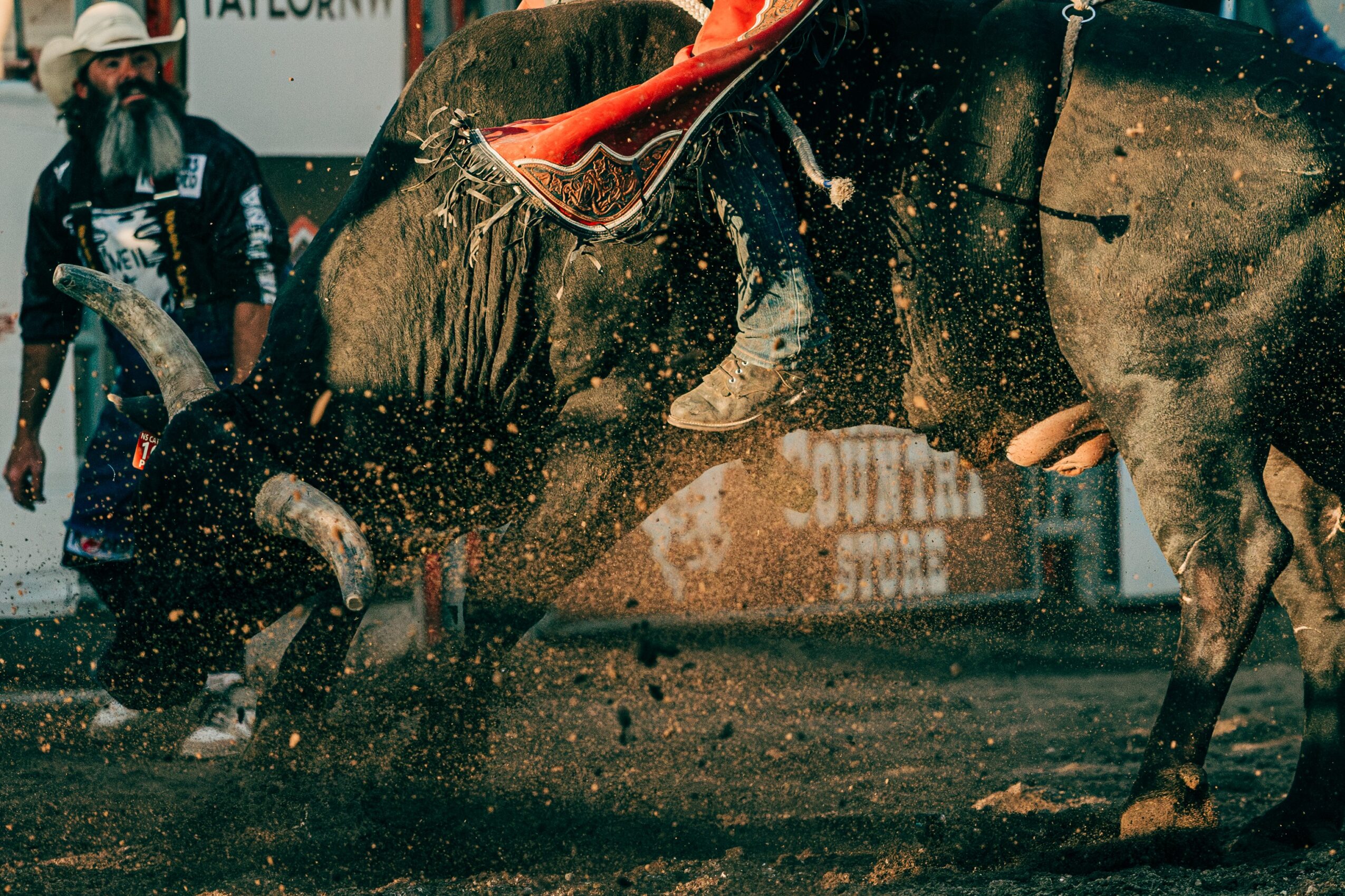 Rodeo scene with a person falling from a bucking horse, dirt flying, and a man in the background watching.