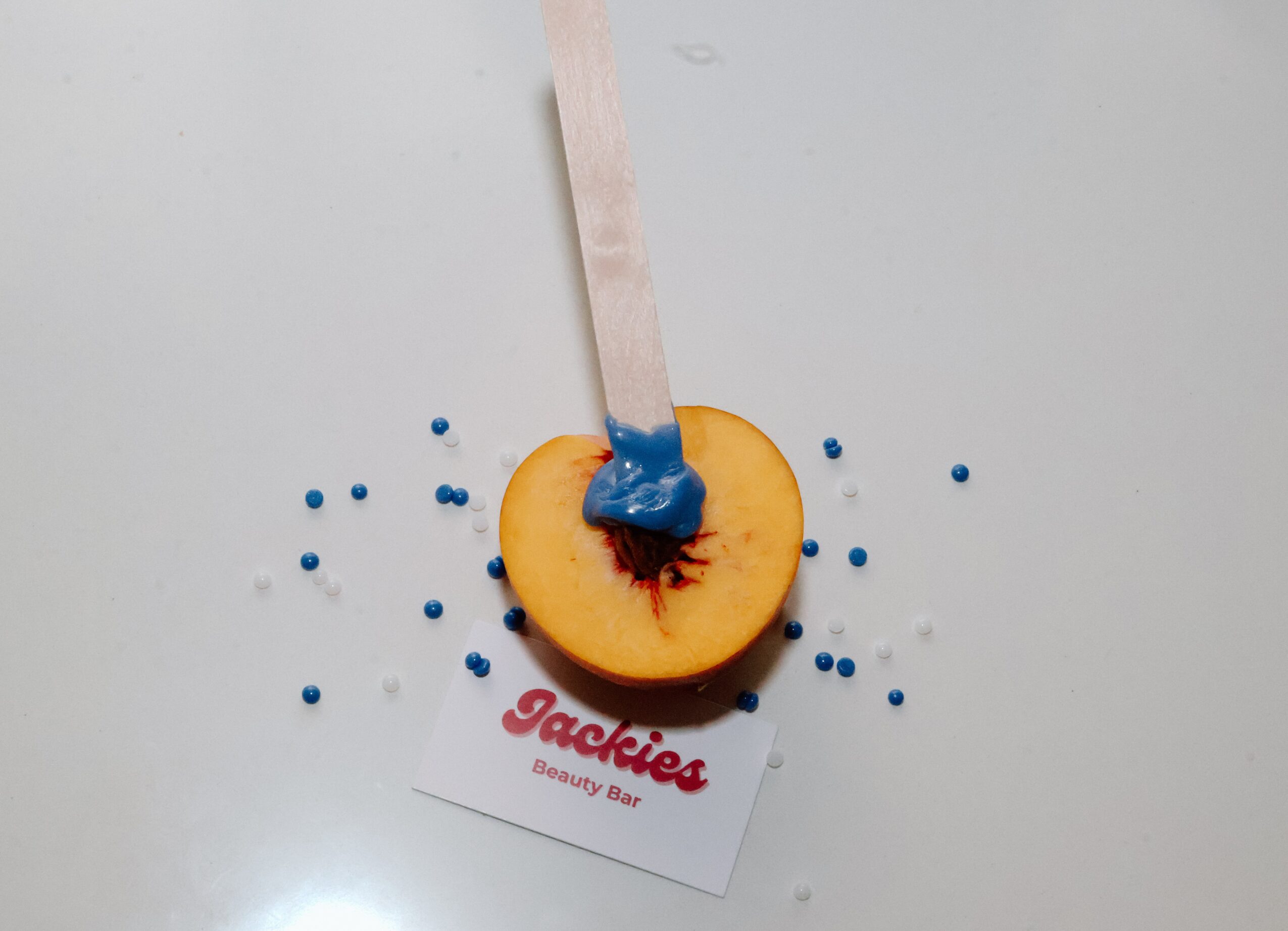 A wooden stick with blue paint rests on a round orange object above a business card, with blue paint drops scattered nearby.