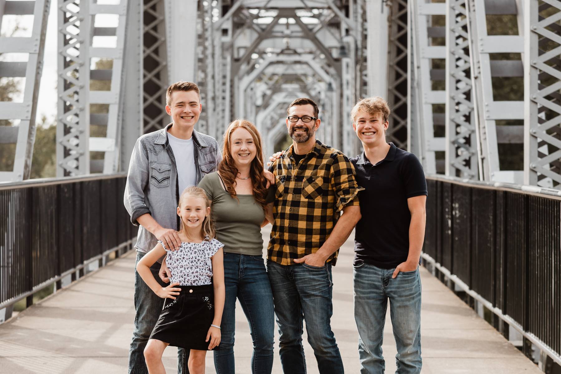 Group of five people, including children, standing on a bridge with metal framework, smiling at the camera.