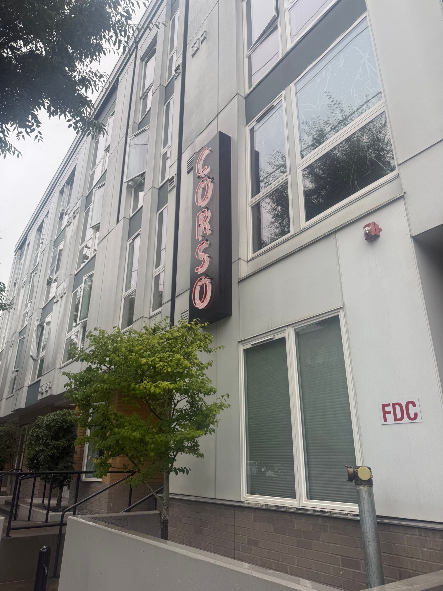 Apartment building facade with windows, a red FDC sign, and a tree beside the entrance.