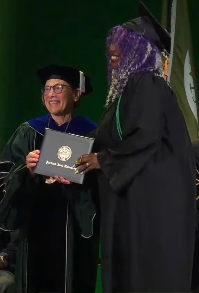 Two people in academic gowns hold a diploma during a graduation ceremony.