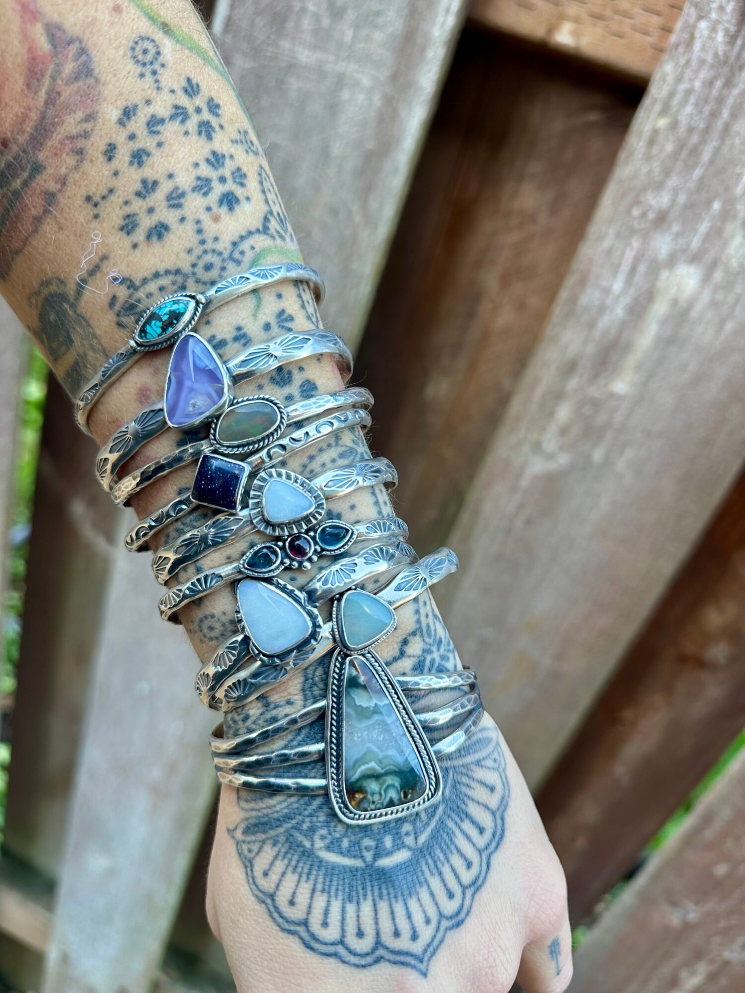 Arm with multiple silver bracelets and a large turquoise pendant, tattooed skin, wooden background.